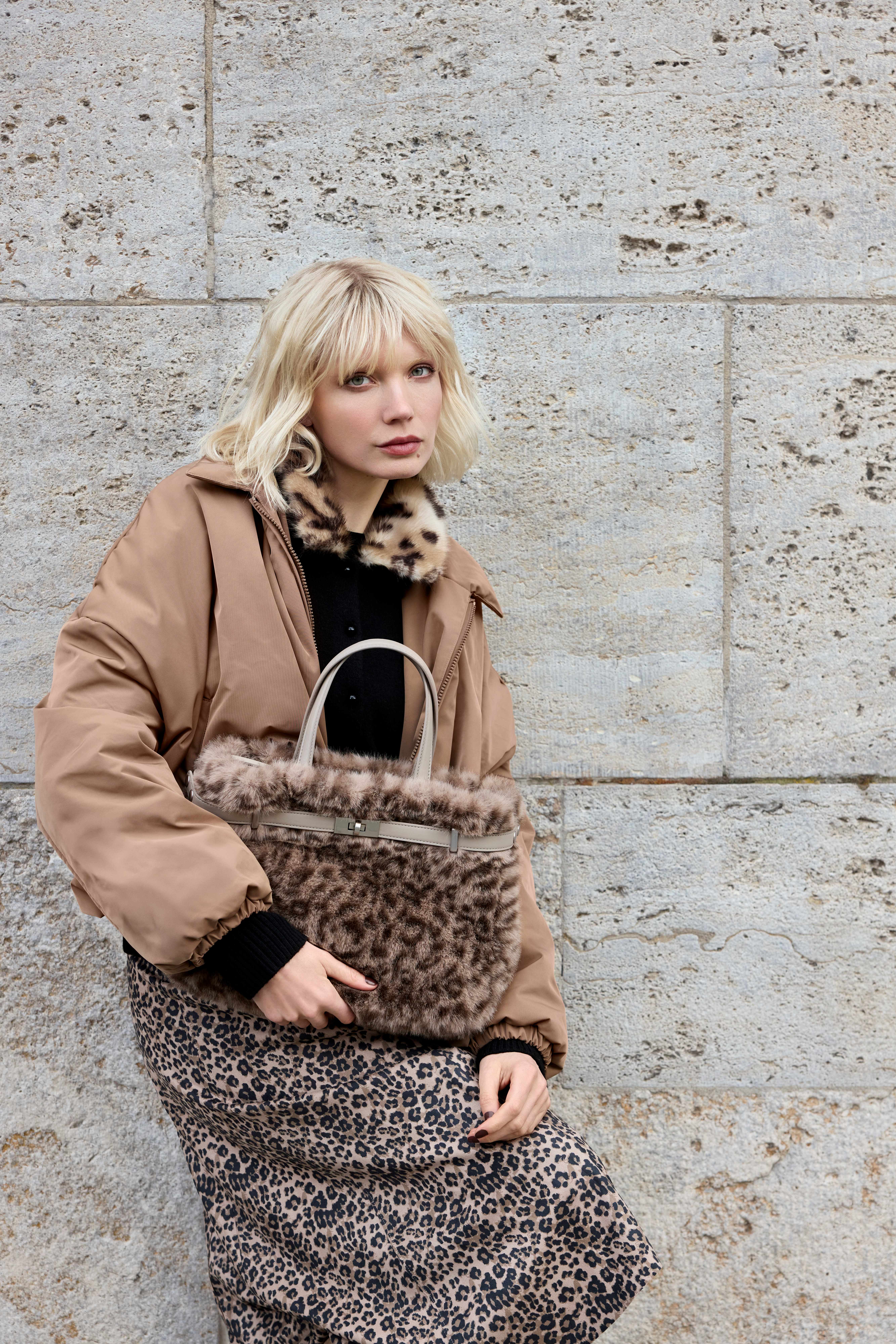 Frau mit kurzem blonden Bob, posiert lässig in einem Leo-Rock mit passender Tasche und einer braunen Jacke