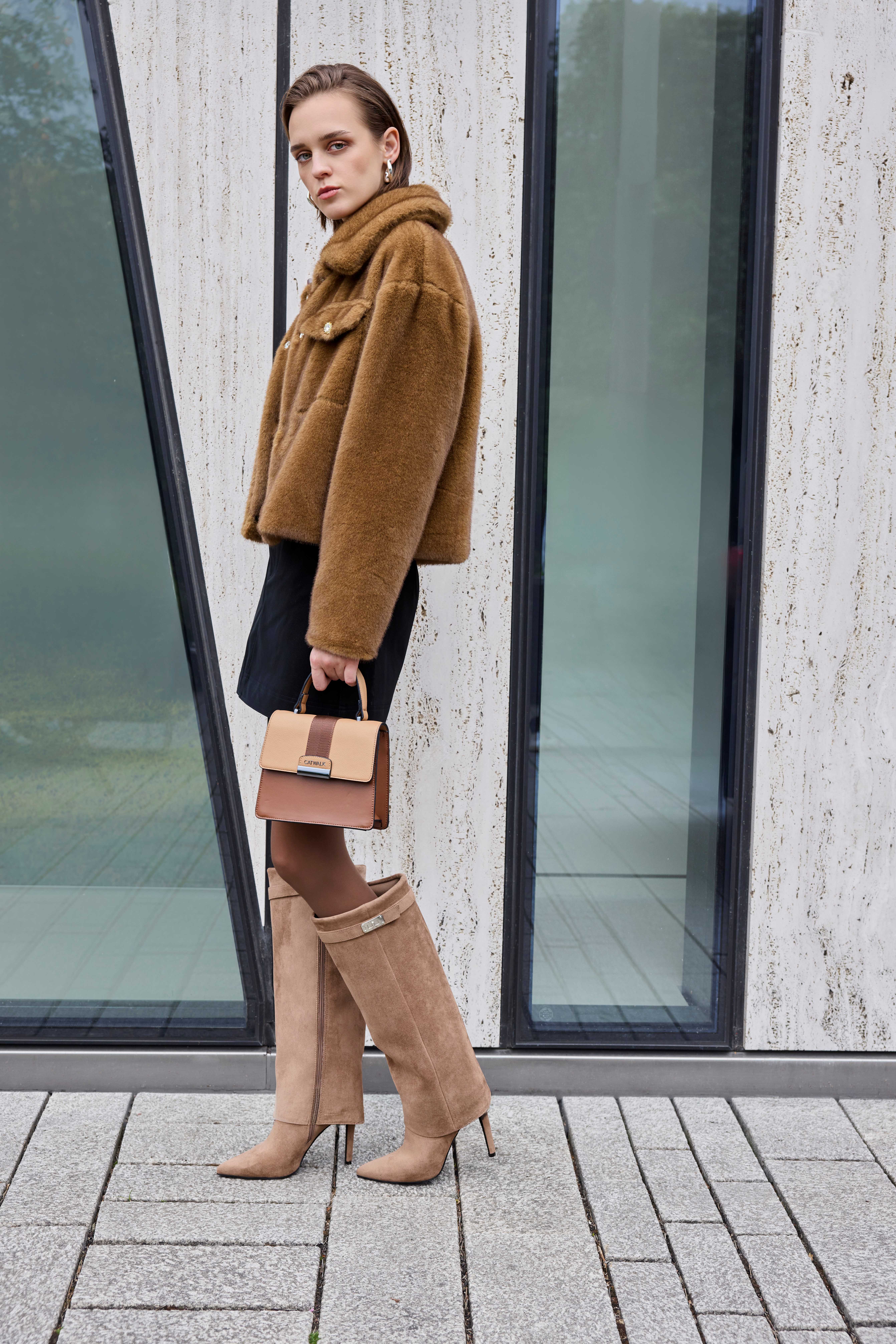 Frau hält hellbraune Tasche, trägt braune Teddyjacke zu schwarzen Rock und Shark Boots