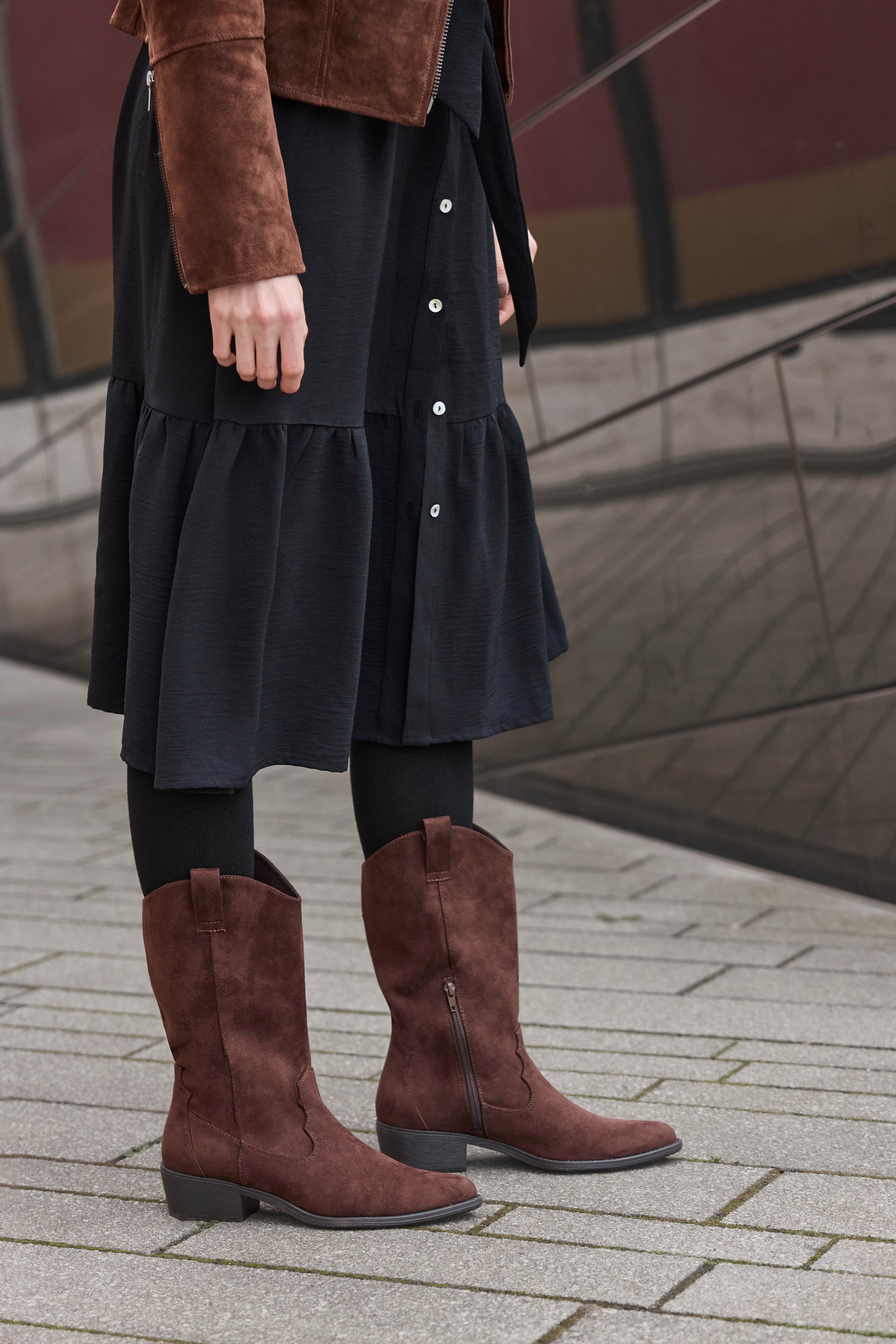 Frau trägt Wildlederjacke, schwarzen Rock und Westernboots
