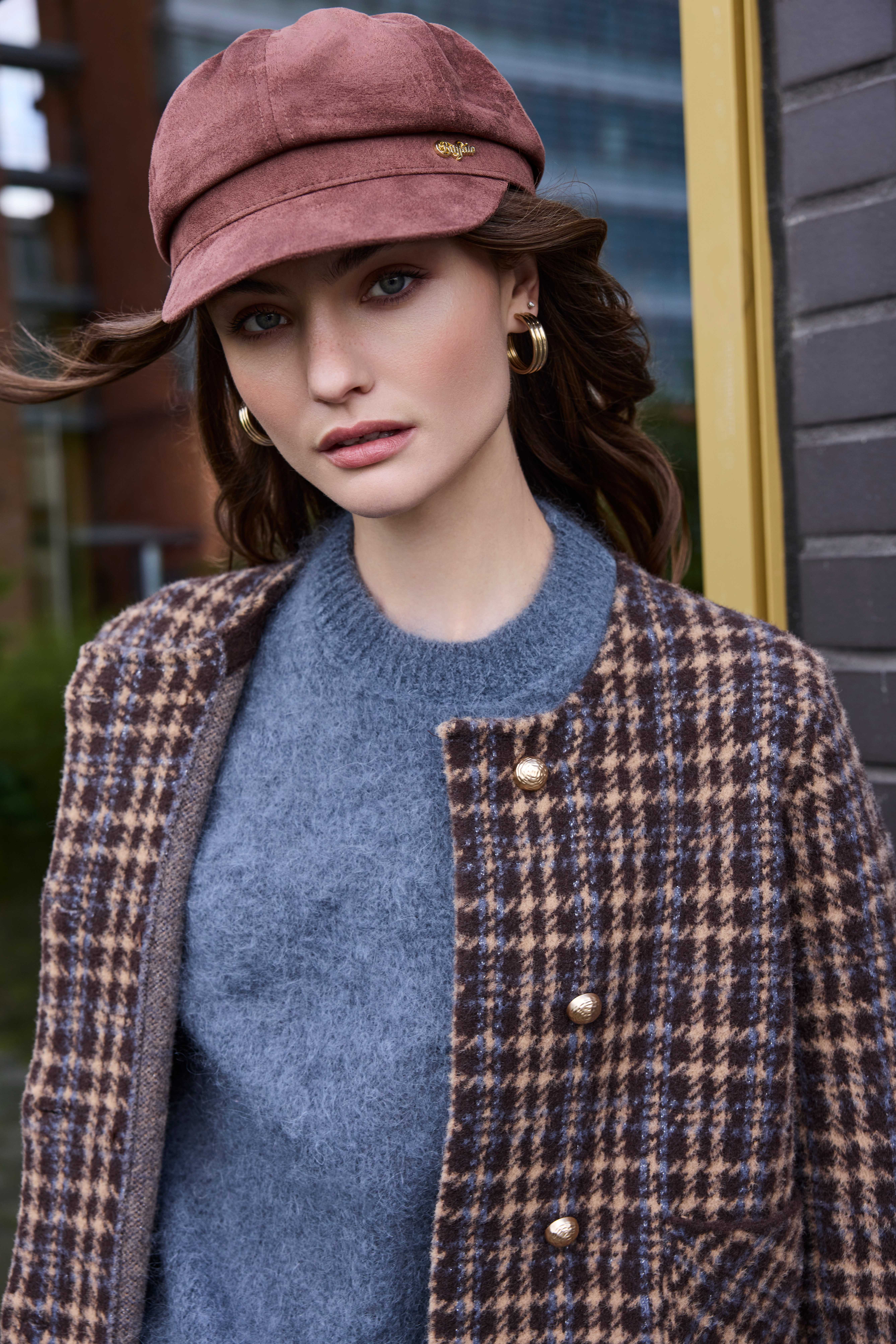 Frau mit rosa Schirmmütze, blauem Pullover und kariertem Wollmantel