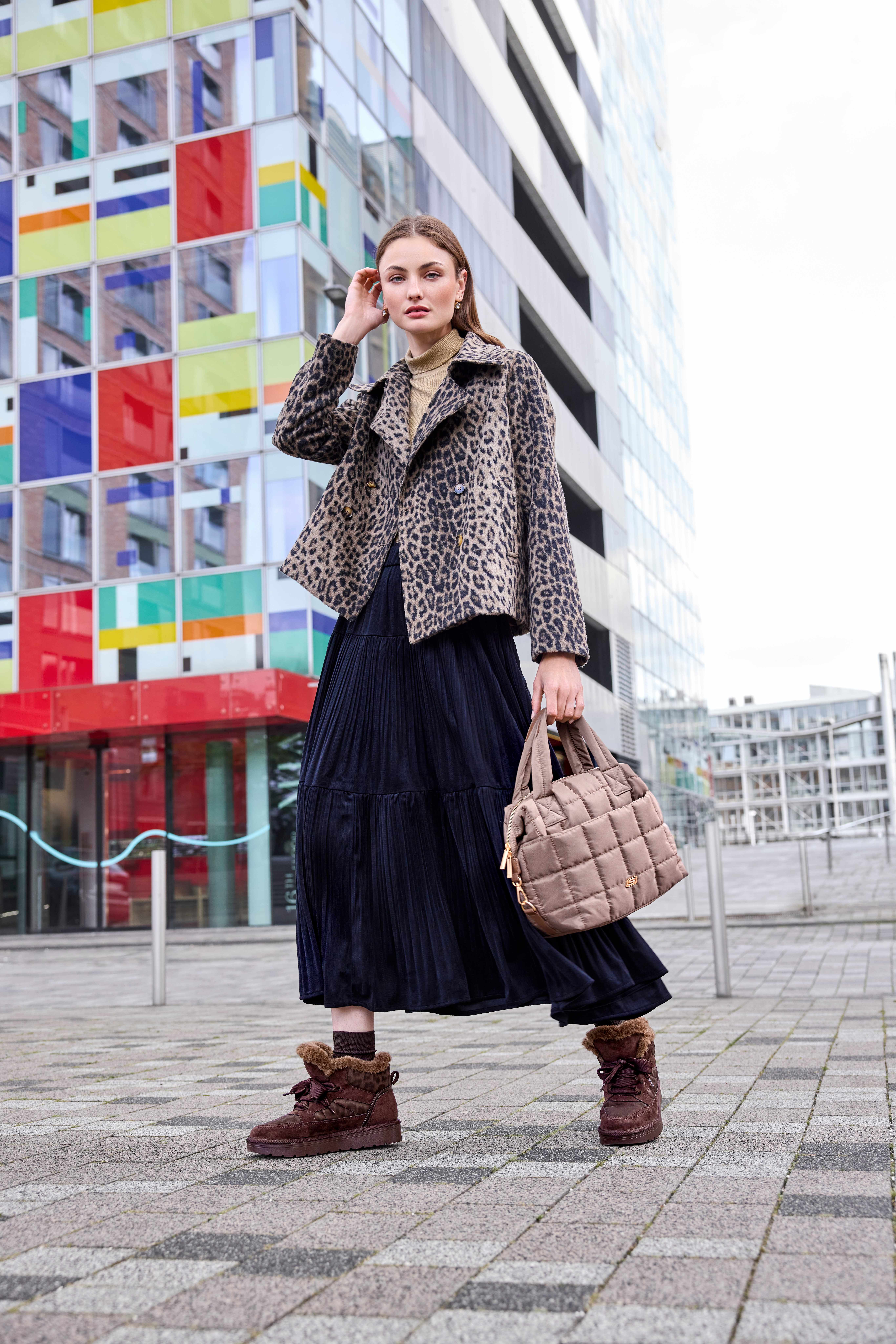 Winterlook mit Leo-Jacke, Plisseerock und gefütterten Winterboots vor bunter Hausfassade