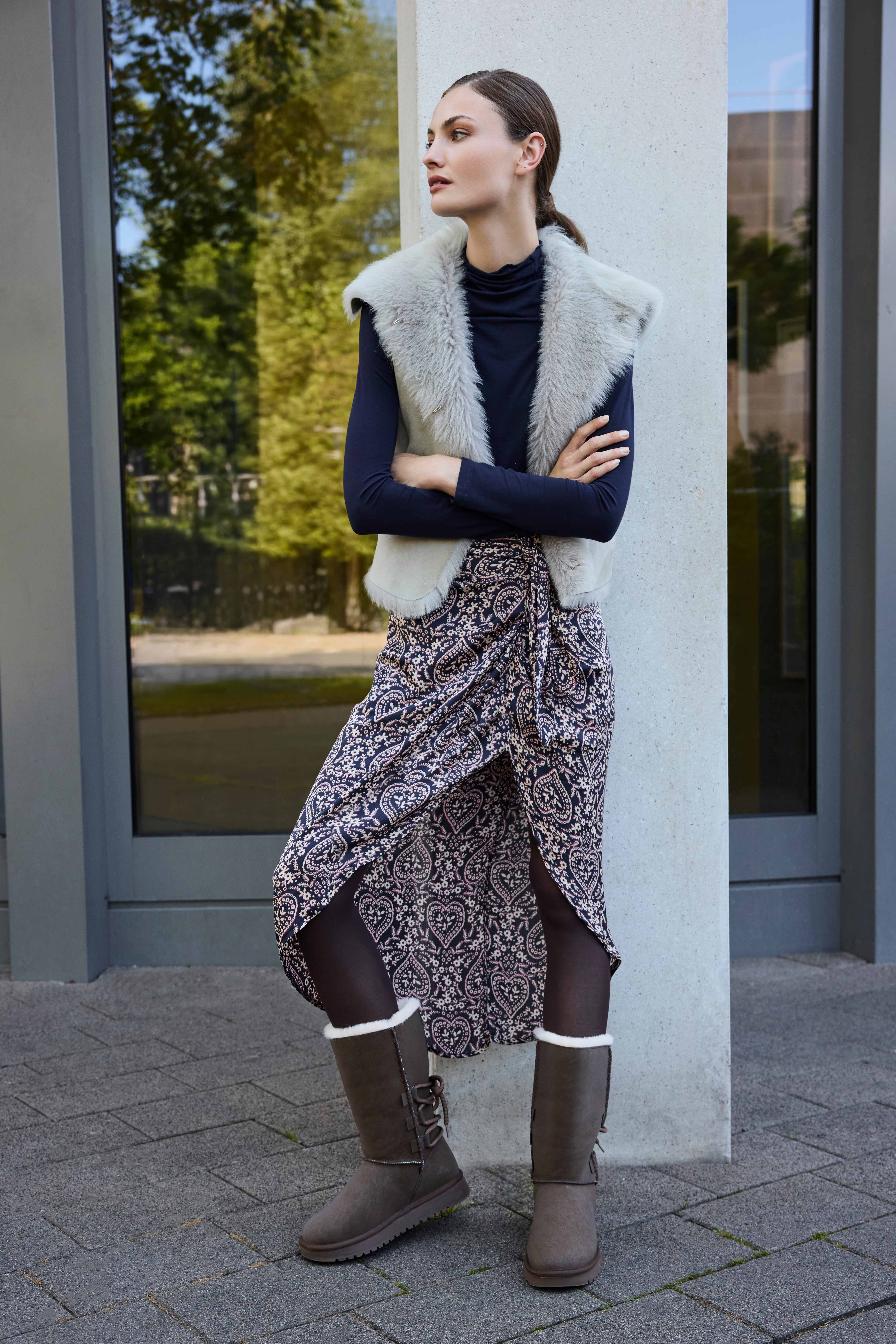 Model in Lammfellweste, Paisley-Rock und gefütterten Winterboots an Betonsäule