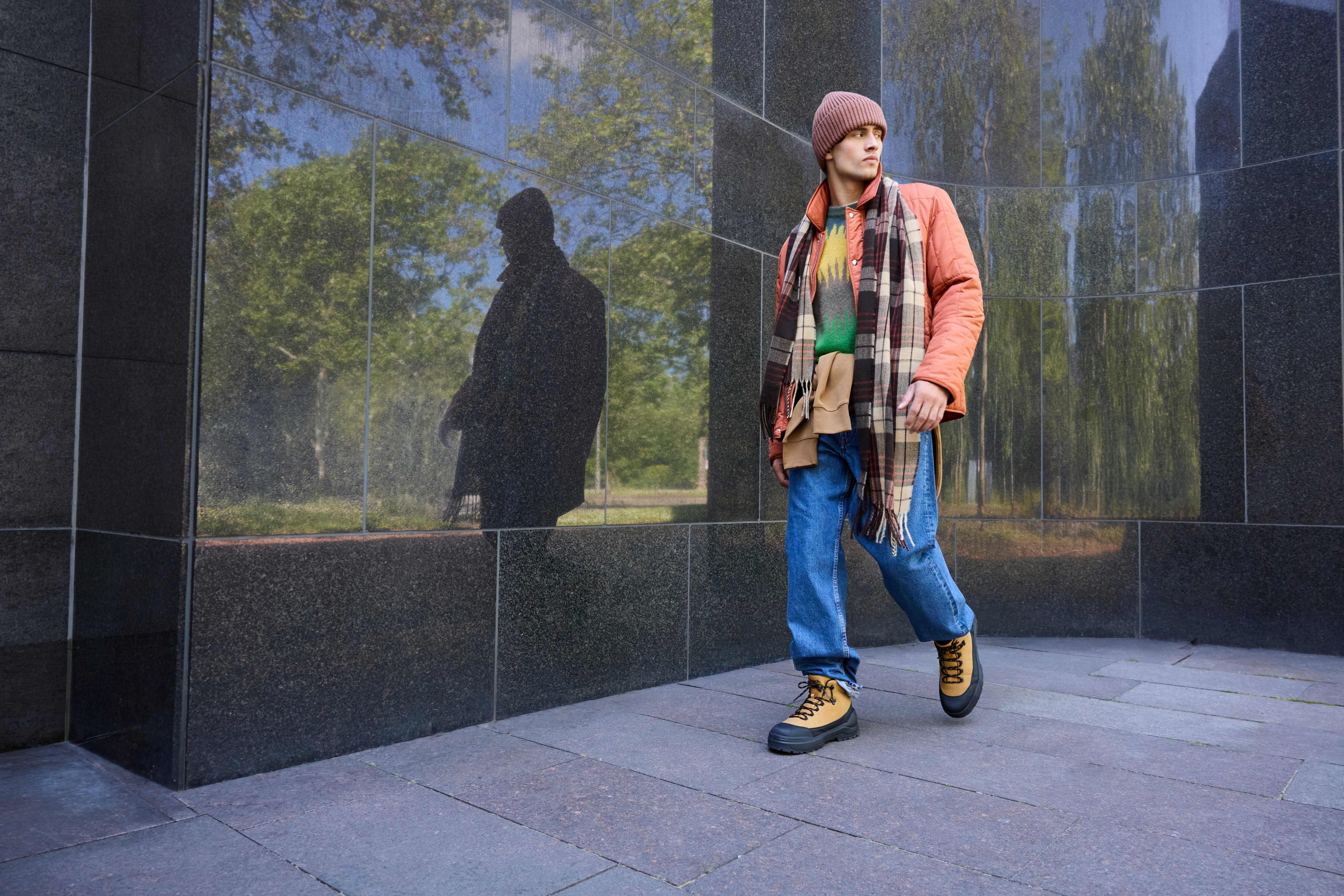 Mann in bunt gemischtem Layering-Look vor schwarzer Marmor-Fassade