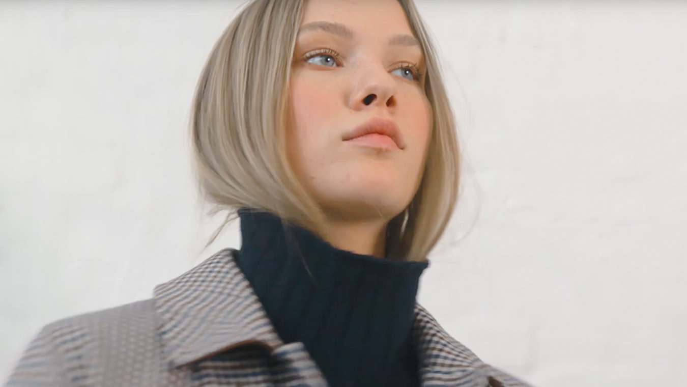 Porträtaufnahme einer Frau mit schwarzem Rollkragenpullover und karierter Jacke, vor weißem Hintergrund