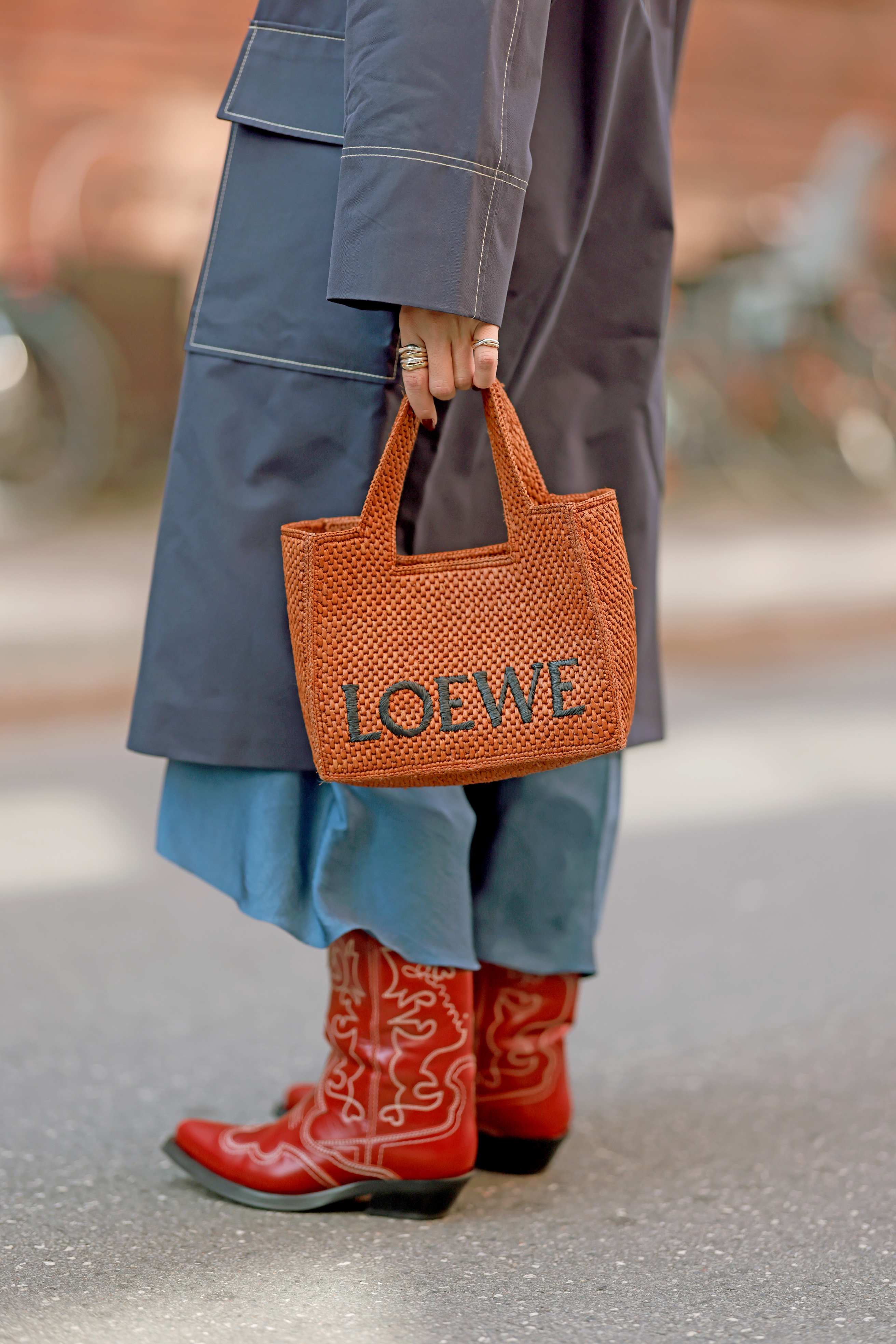 Person trägt rote Cowboystiefel als Statement-Schuhe, kombiniert mit einem dunkelblauen Mantel und einer braunen LOEWE-Handtasche