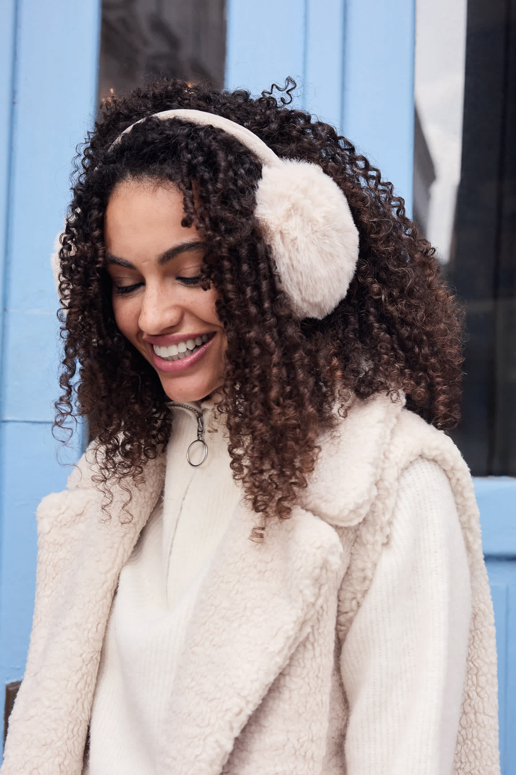 Lächelnde Frau mit hellem, flauschigem Oberteil und flauschigen Kopfhörern