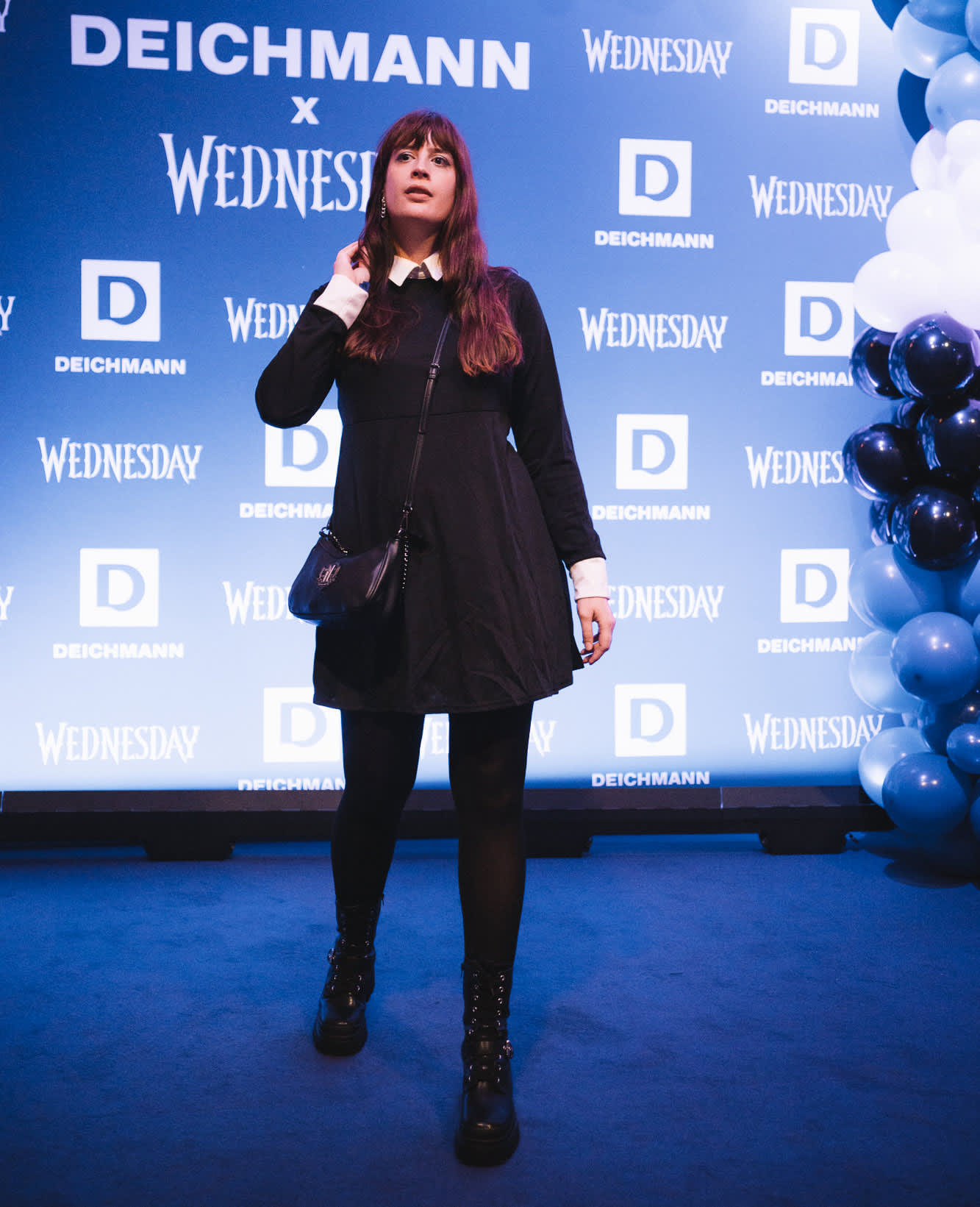 Frau auf einem Wednesday-Event der Marke Deichmann, gekleidet in ein typisches Wednesday-Outfit, mit Sponsoren-Wand im Hintergrund