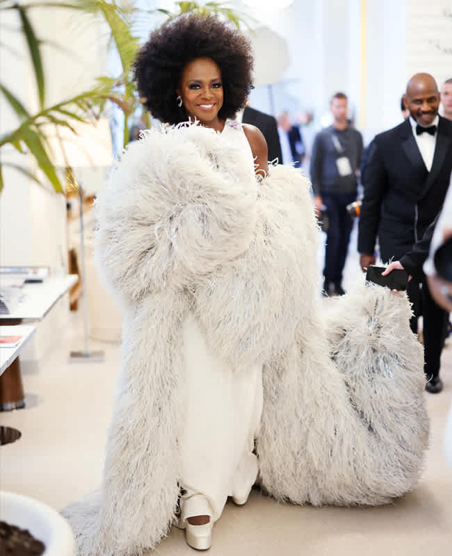 Frau mit schwarzen Haaren und weißem Kleid in einem buschigen Fake Fur-Mantel