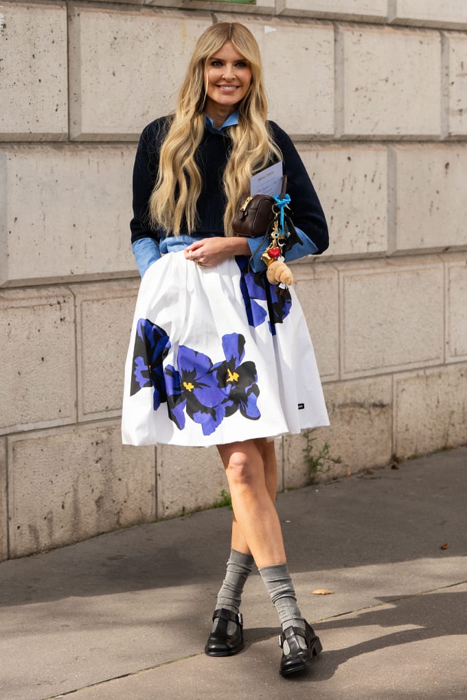 Lächelnde Frau trägt Outfit-Kombination aus schwarzem Top und weißem Rock mit dezentem Blumen-Muster