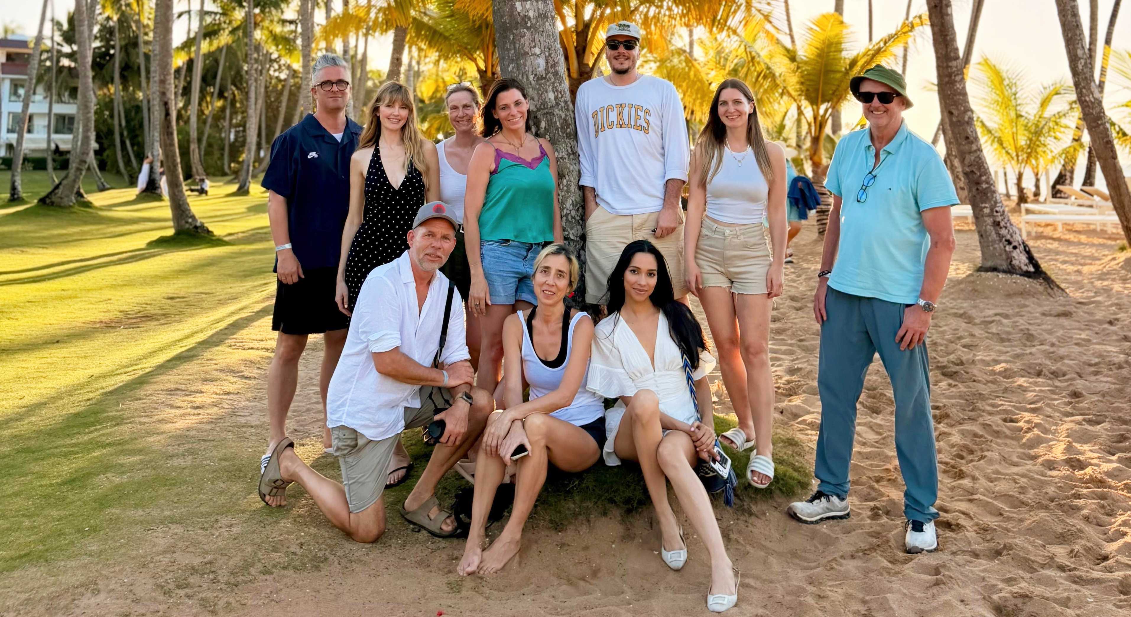 Deichmann-Team aus Männern und Frauen posiert sommerlich vor Palmenkulisse