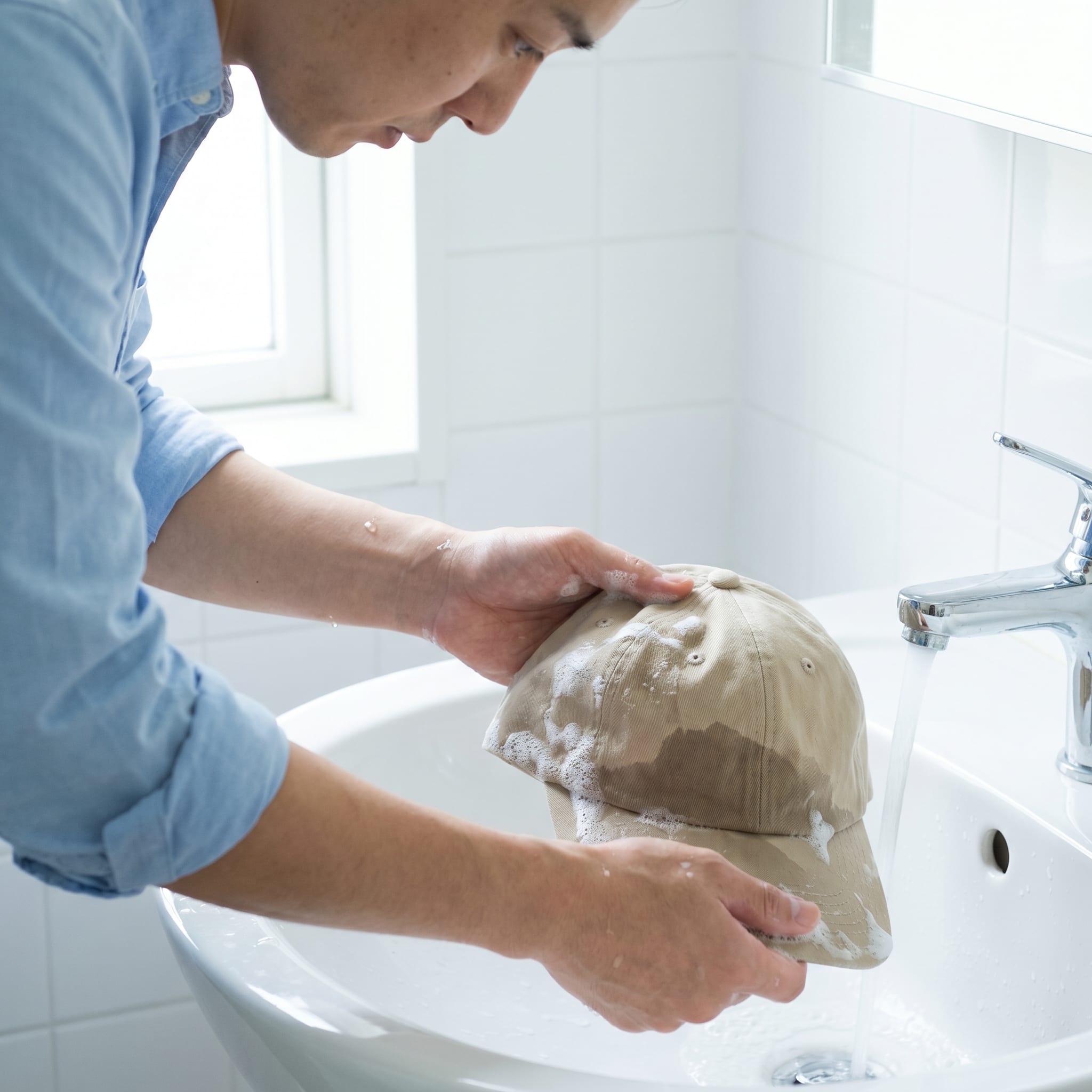 Mann wäscht Kappe per Hand unter Wasserhahn
