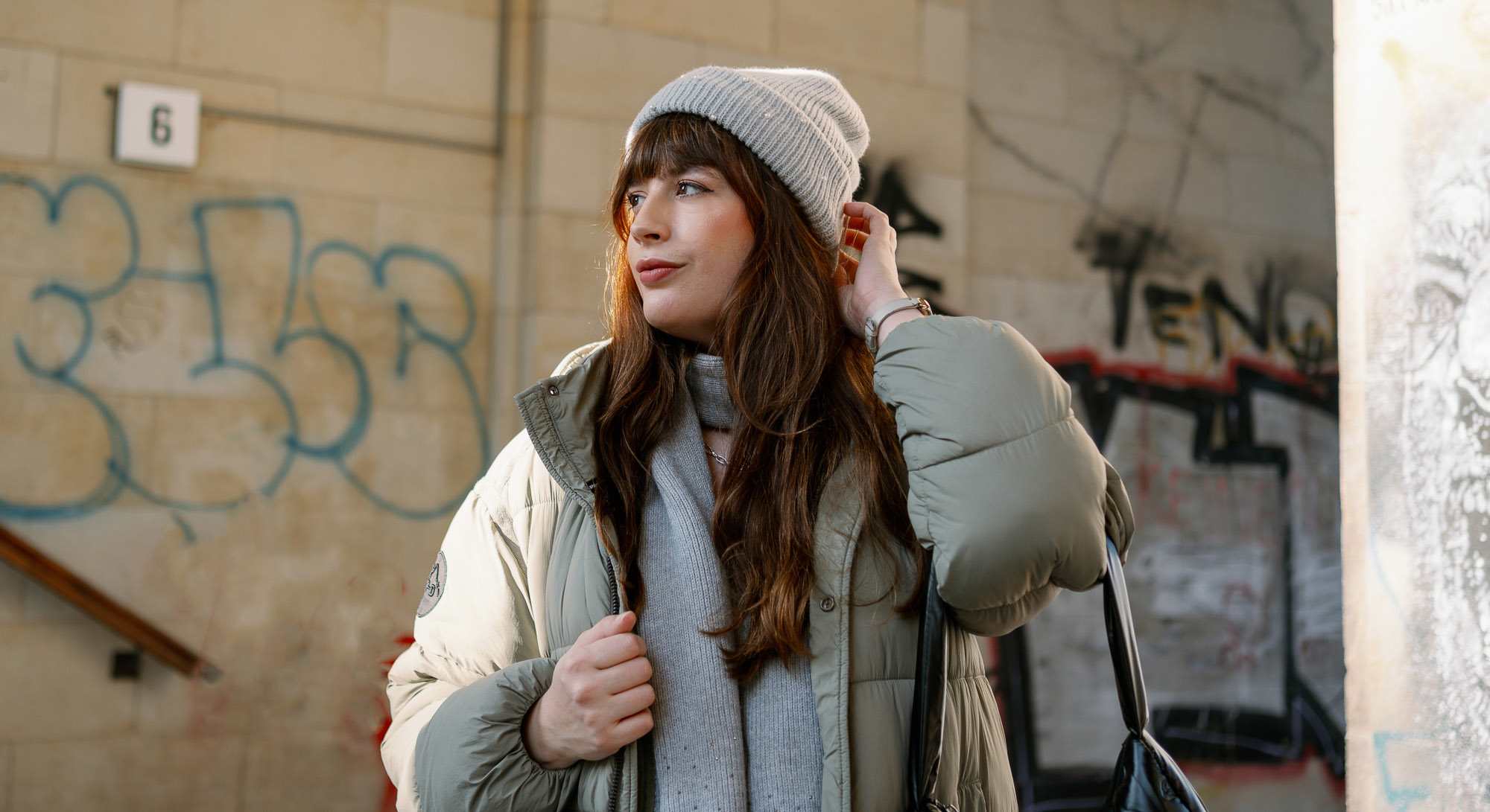 Frau mit Oversize-Mantel, grauem Schal und passender Mütze, stehend in urbaner Kulisse