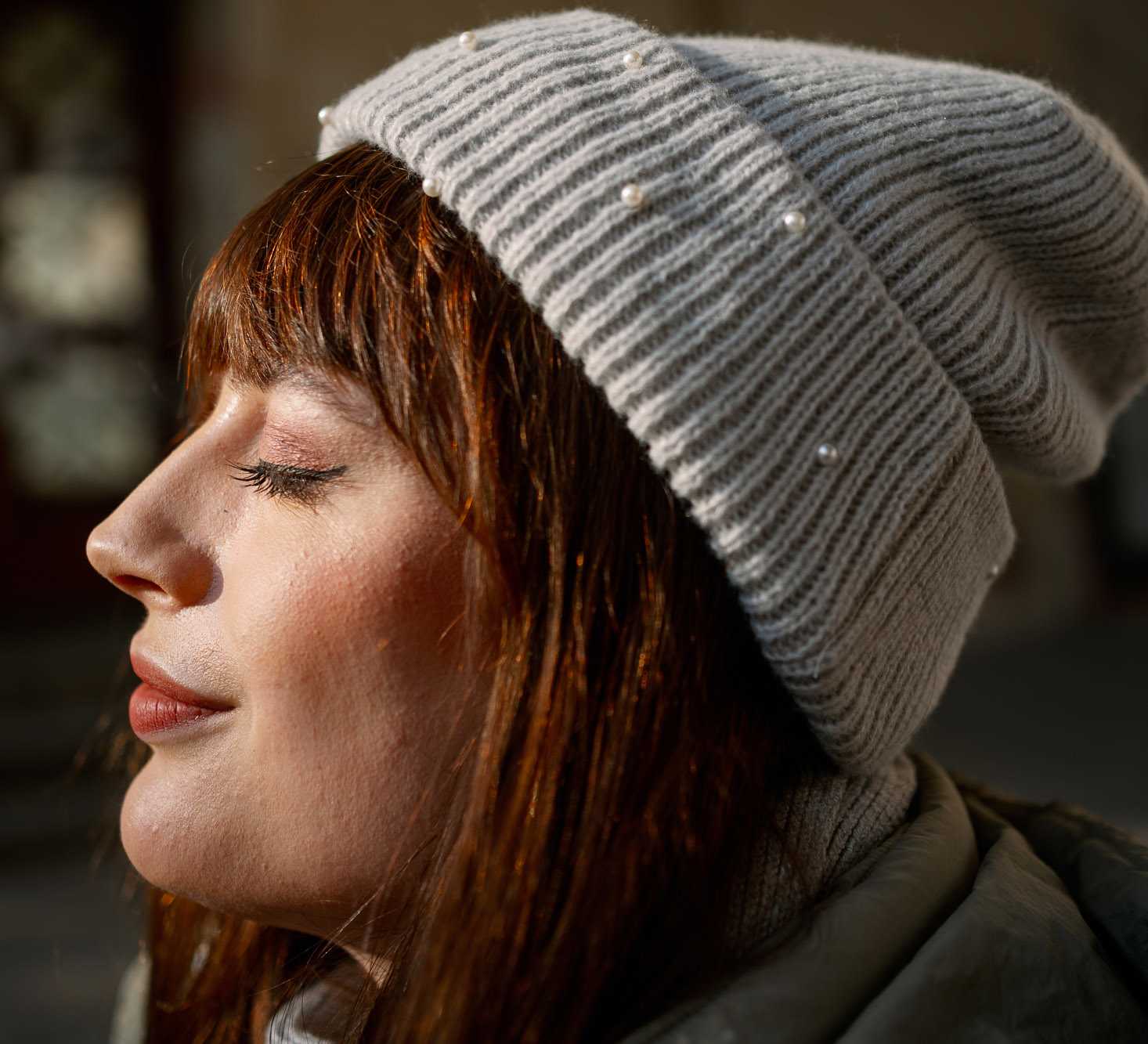 Junge Frau, mit entspanntem Gesichtsausdruck und grauer Strickmütze, genießt Sonne auf ihrem Gesicht