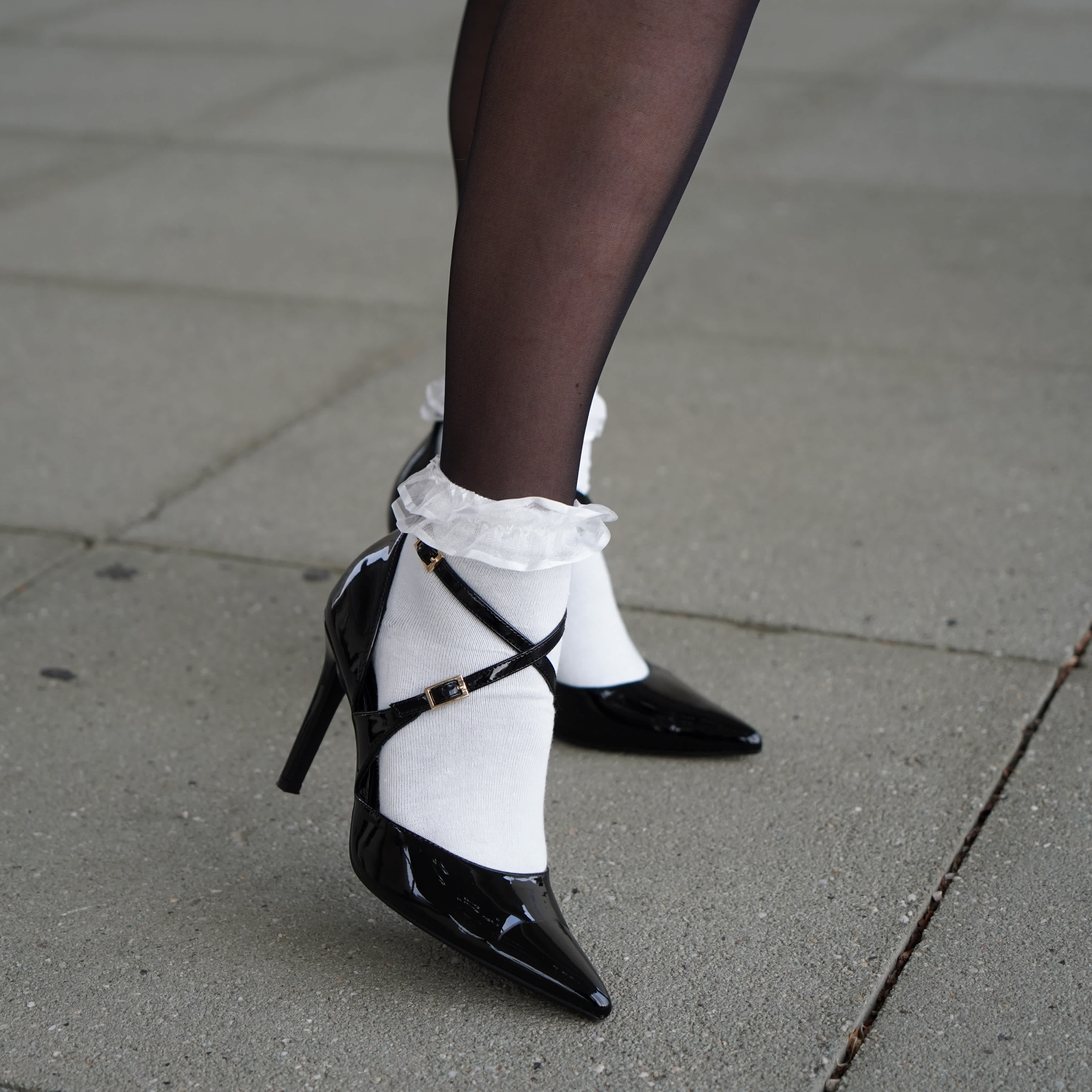 Person trägt schwarze Lack-Pumps mit weißen Strümpfen und Rüschen