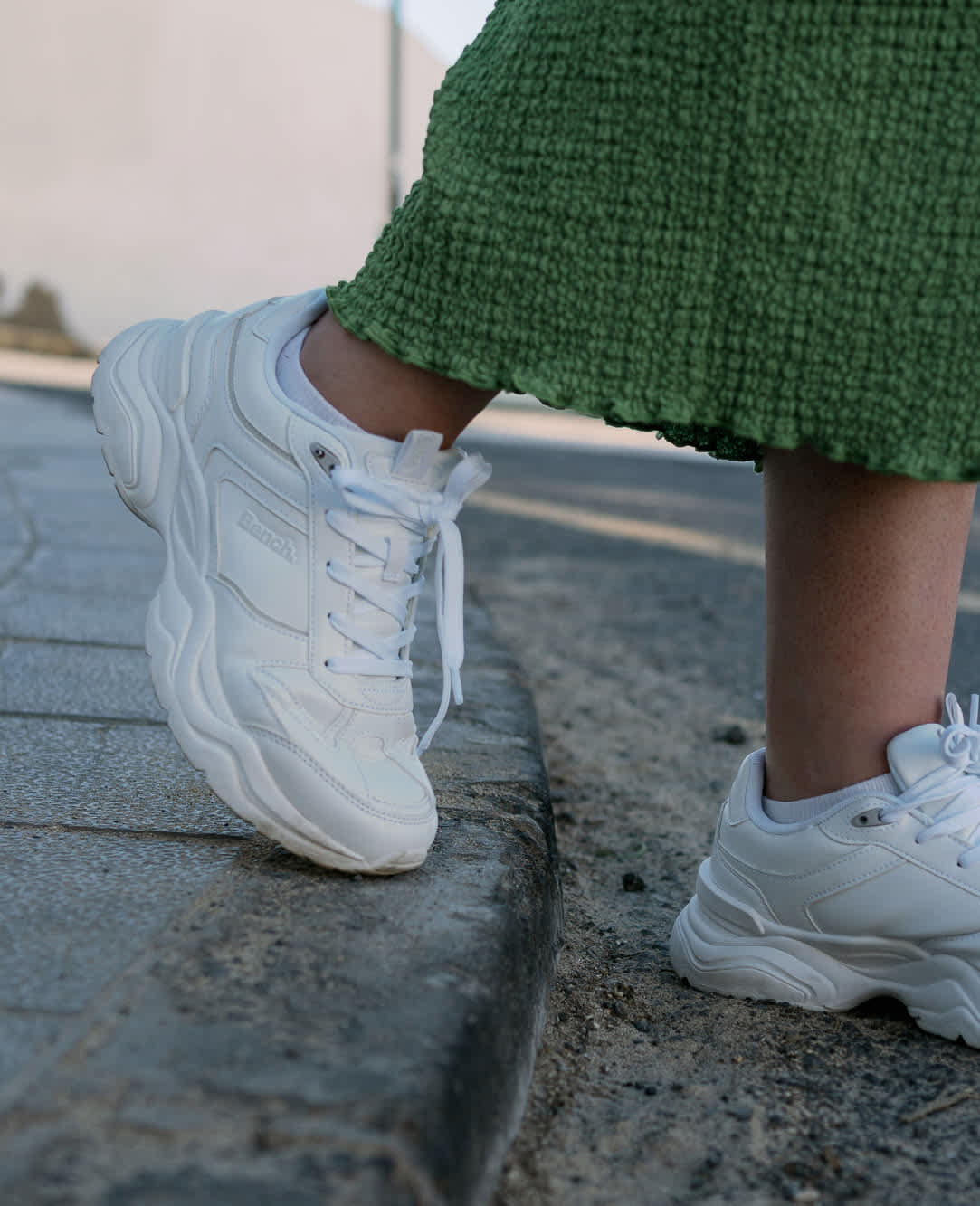 Nahaufnahme von weißen Sneaker-Schuhen, getragen von einer Frau in grünem Kleid