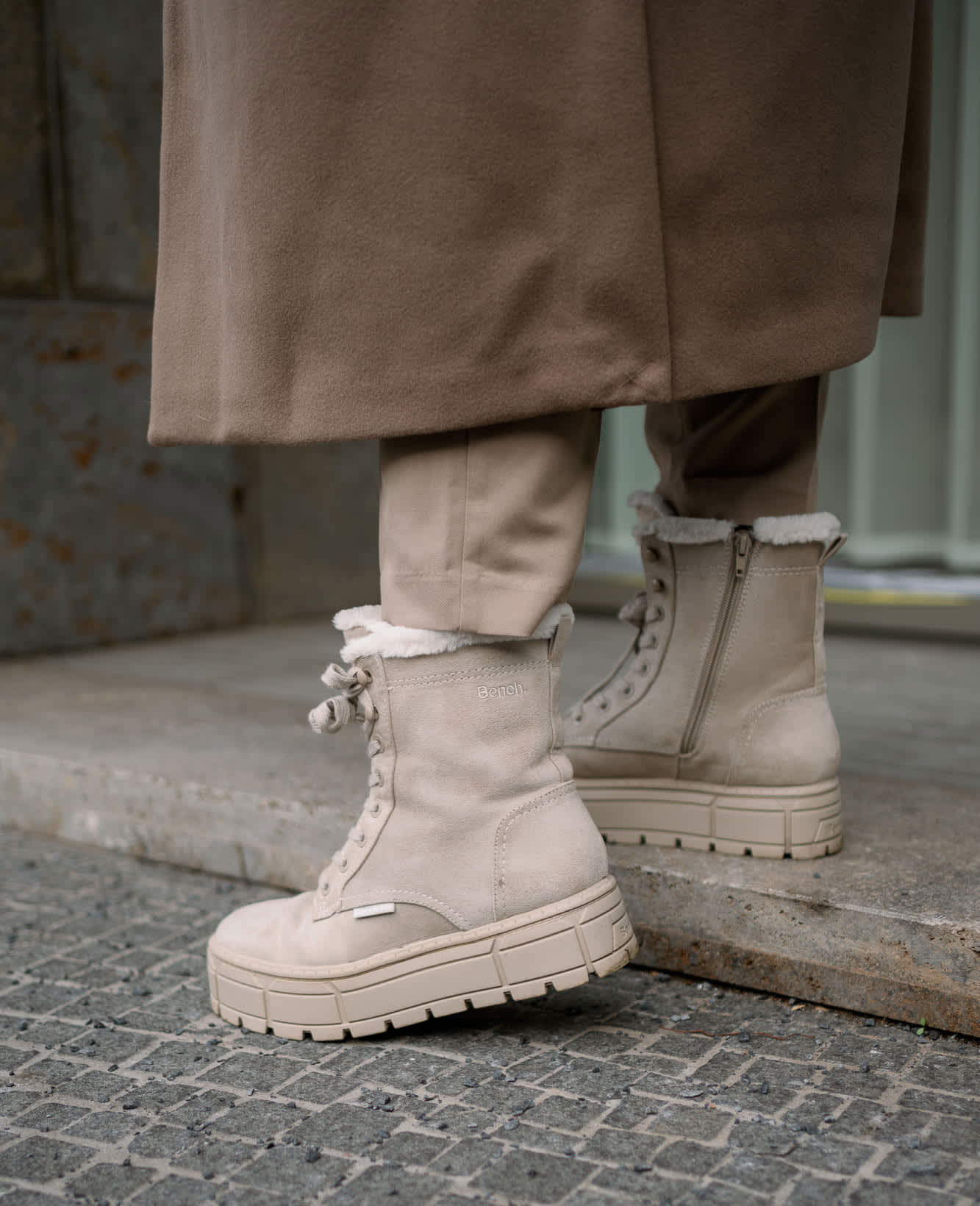 Nahaufnahme einer Frau, die beige Boots zu einem langen Mantel trägt