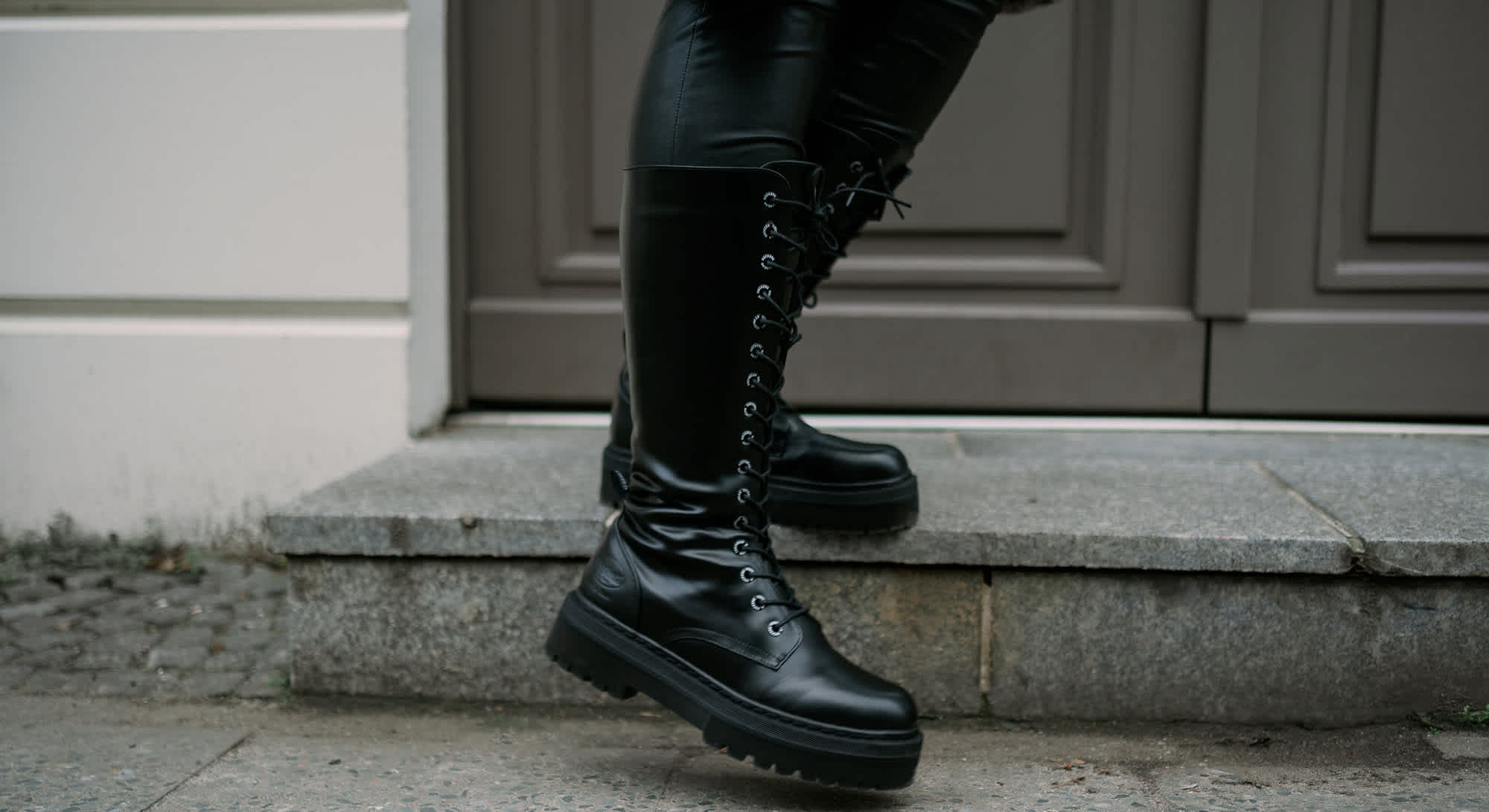 Nahaufnahme einer Person mit schwarzen Dockers Schnürstiefeln von DEICHMANN, stehend auf Treppenabsatz