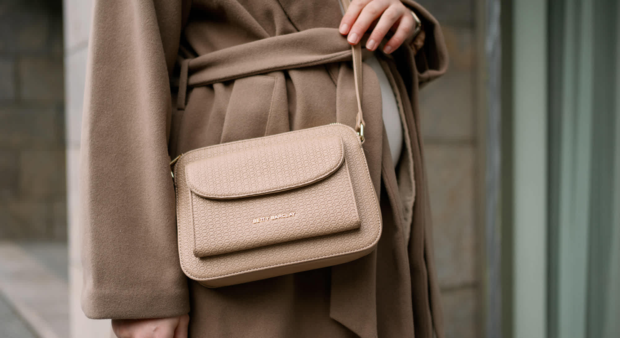 Frau in bodenlangem beigen Mantel trägt braune Betty Barclay-Handtasche