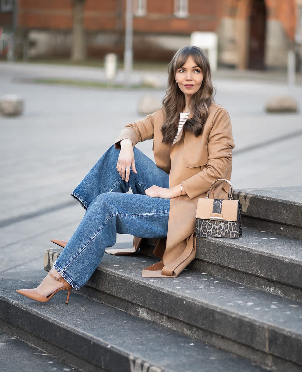 Frau mit braunem Mantel und blauer Jeans sitzt auf Steintreppe