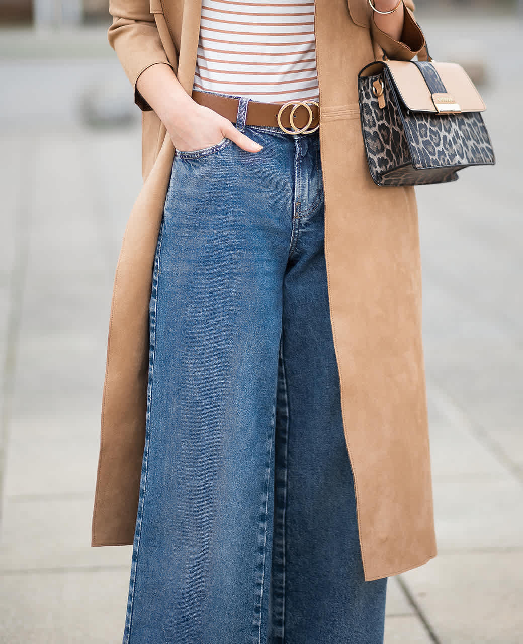 Frau trägt Outfit aus braunem Mantel und blauer, weiter Hose samt Handtasche