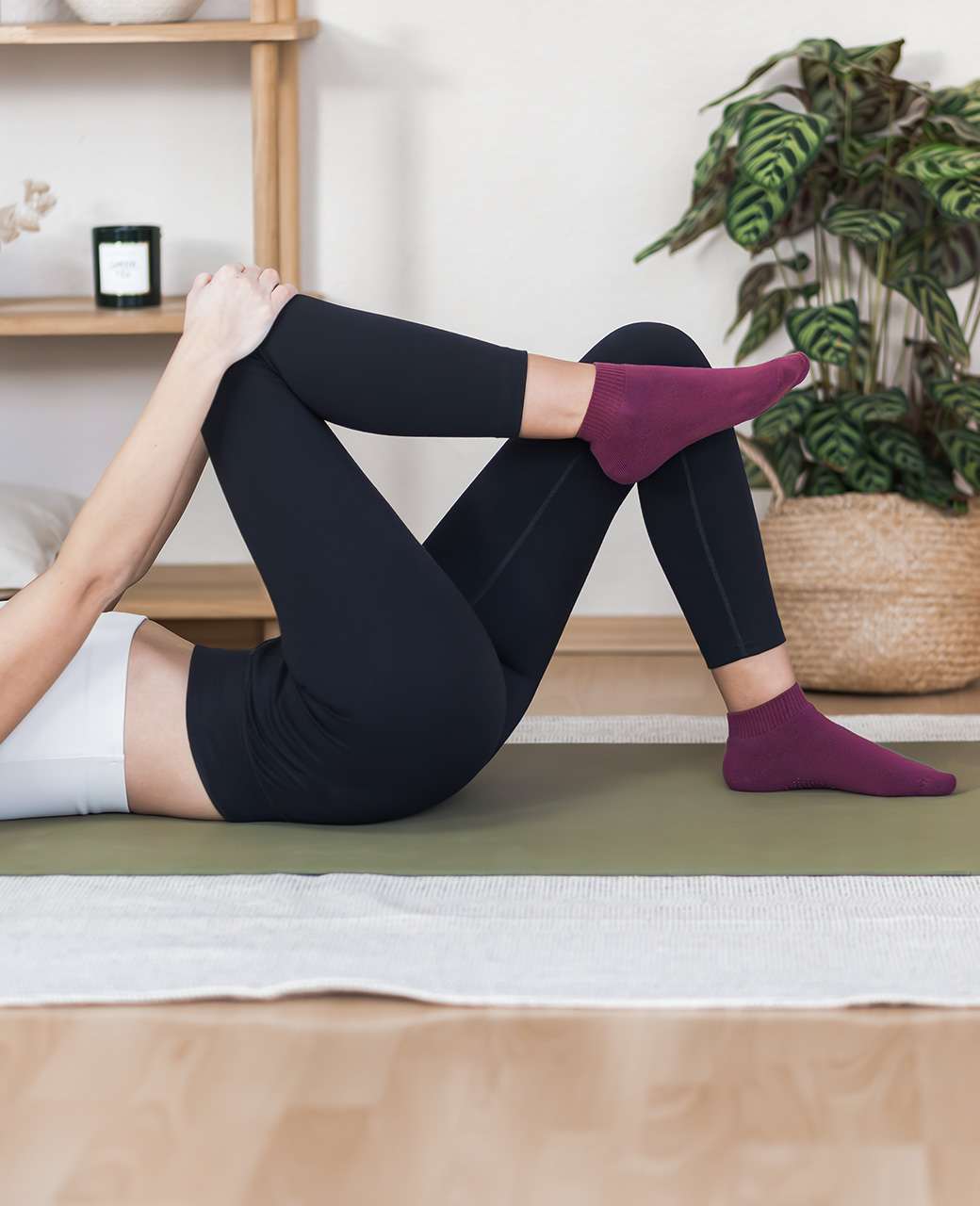 Frau liegt auf Yogamatte und führt Übung aus, trägt weißes Top & schwarze Yogapants