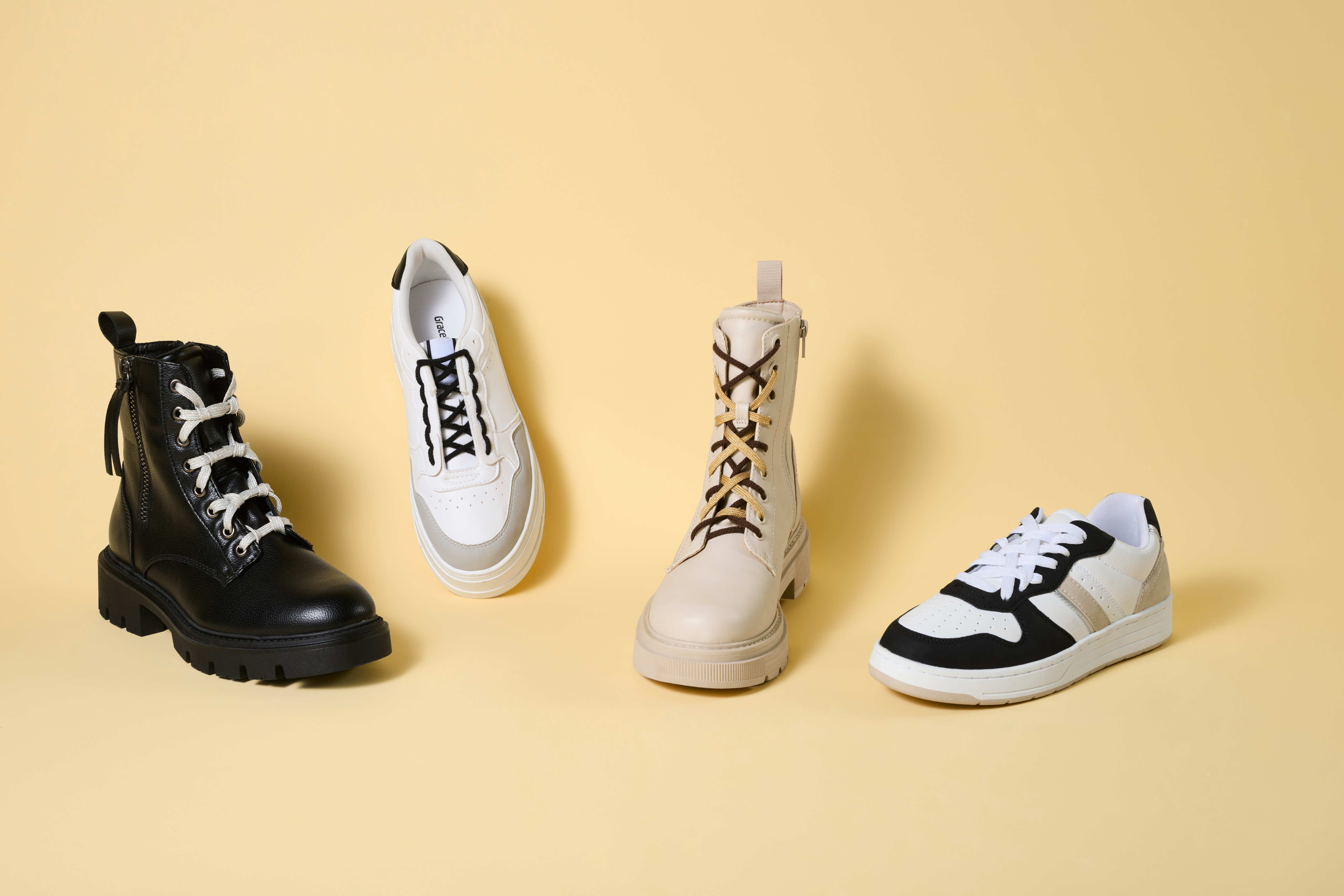 Vier einzelne Schuhe mit gebundenen Schnürsenkeln, stehend vor gelbem Hintergrund