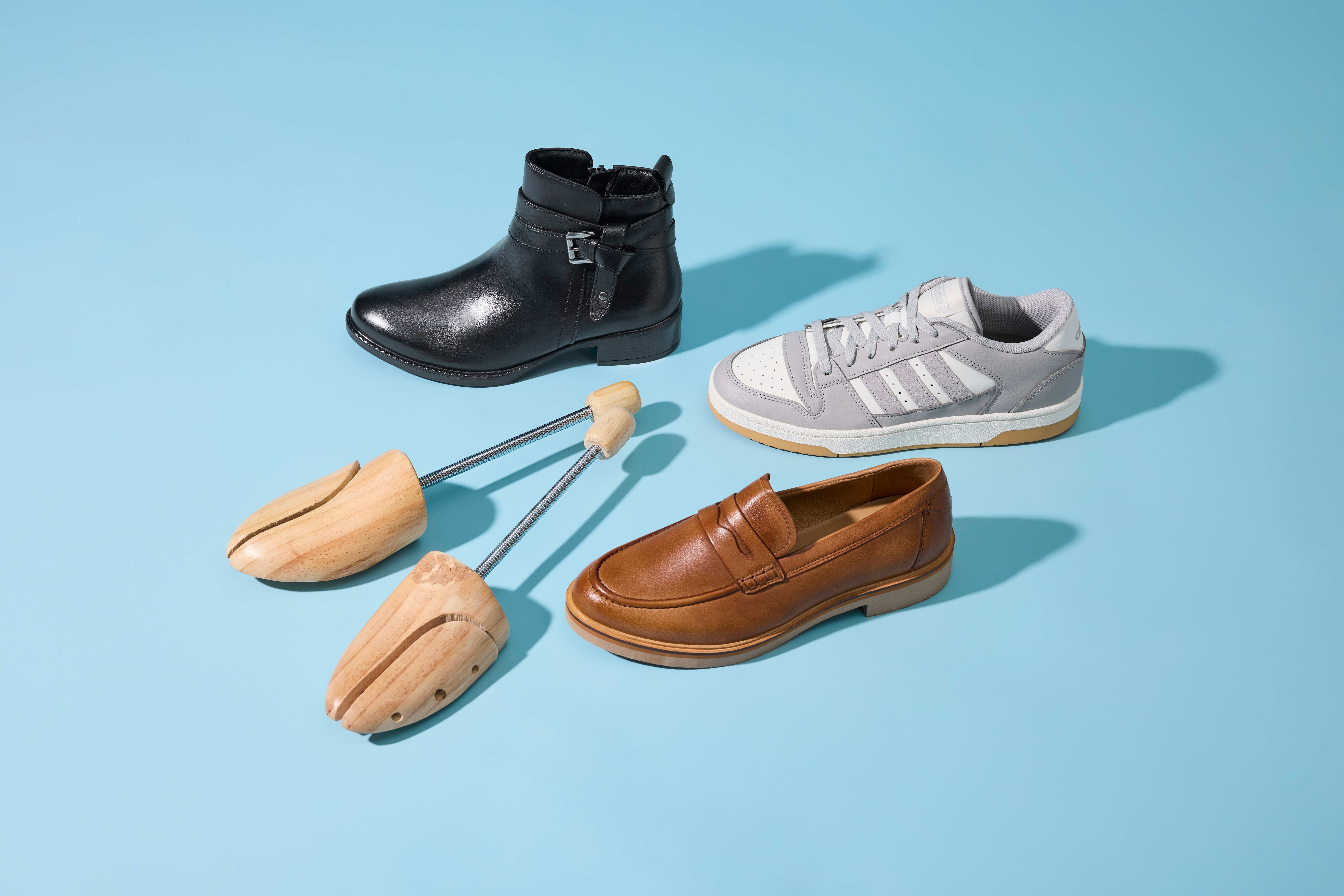 Tre scarpe in pelle, tessuto e materiale tessile sono disposte attorno a un tendiscarpe di legno