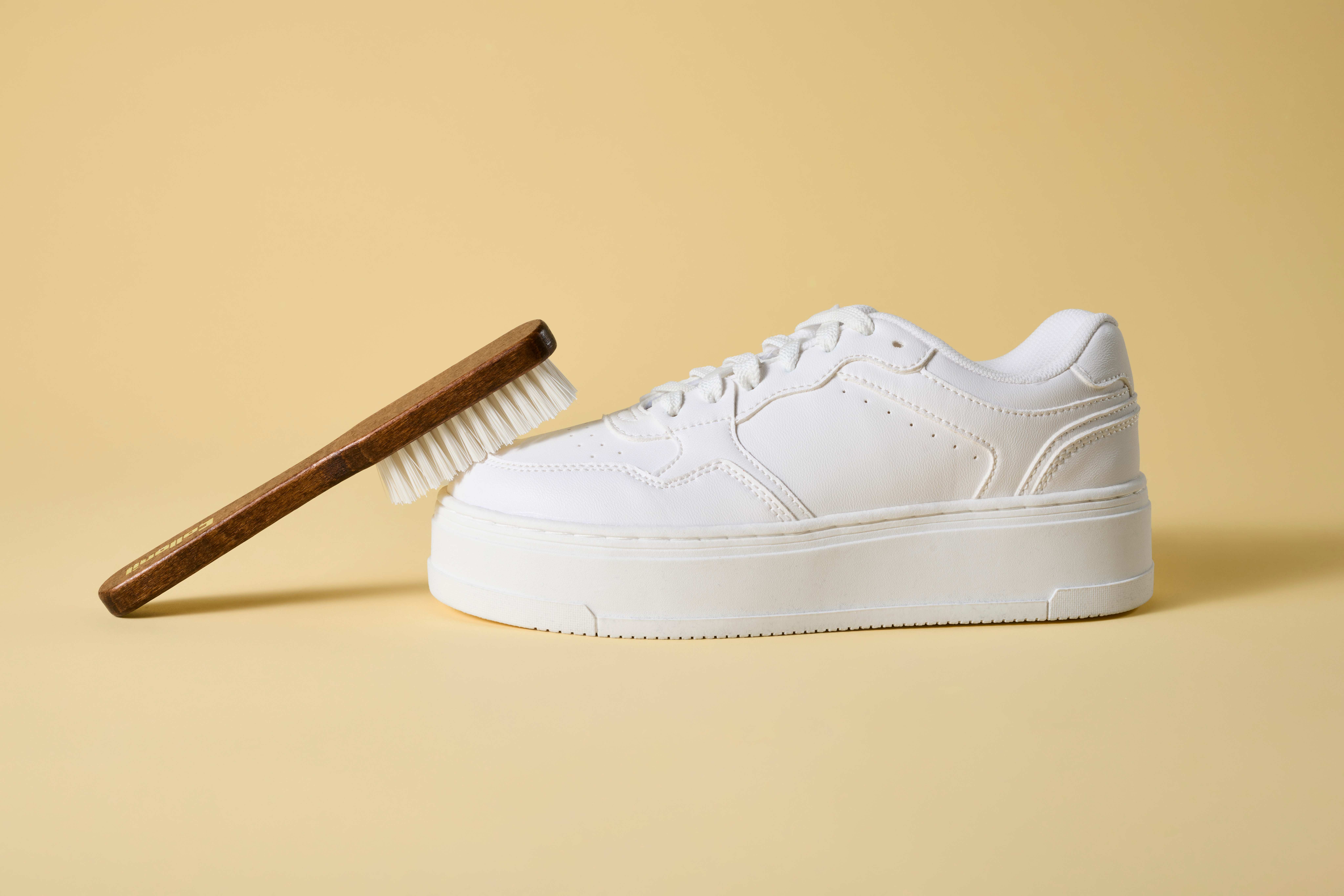 Schwarze Schuhbürste lehnt zum Putzen an weißem Sneaker