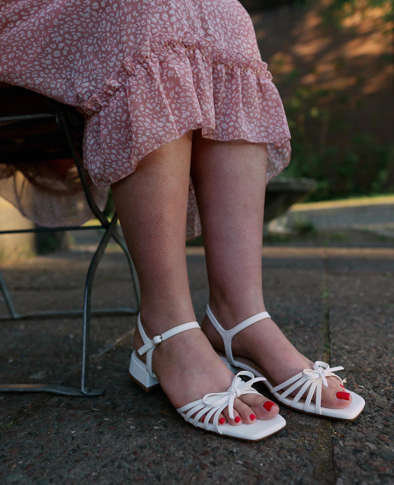 Frau in pinkem Kleid trägt dazu weiße Sandalen mit feinen Details