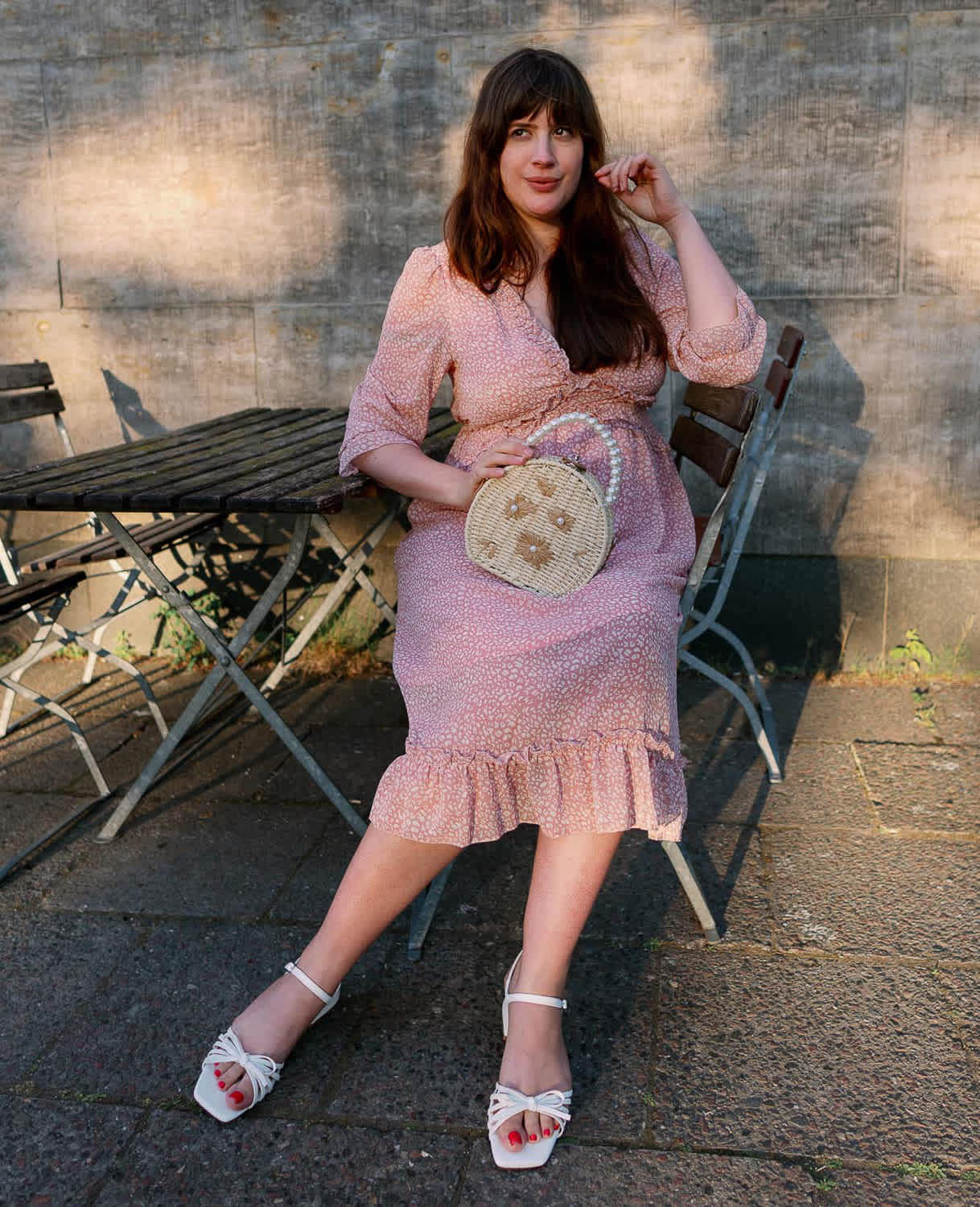 Frau sitzt auf Bank, in pastellfarbenem Kleid, mit Blumenstrauß in der Hand