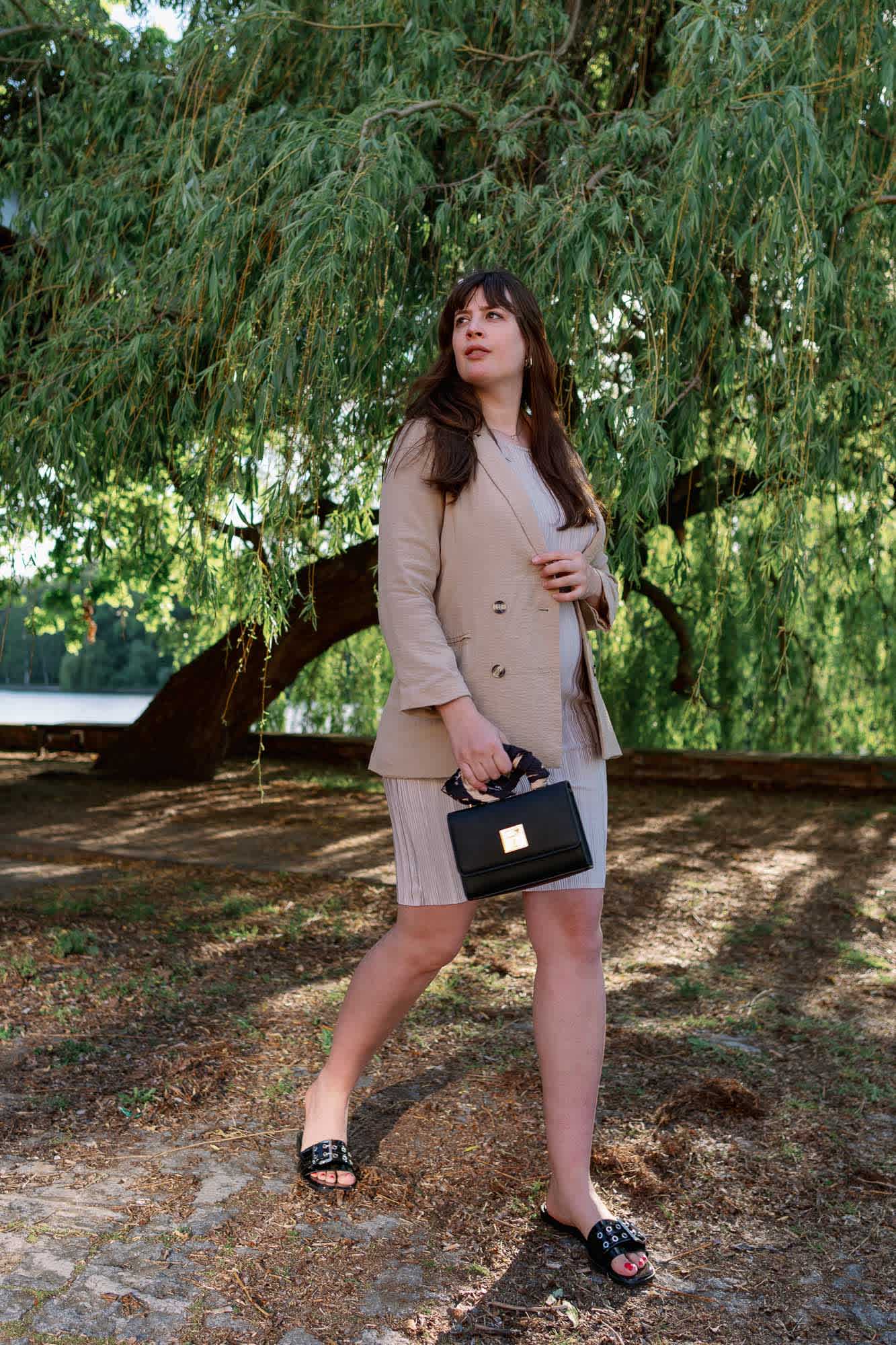 Frau in gediegenem Outfit für Hochzeitsgäste, klassischer Blazer und Rock mit schwarzer Handtasche 