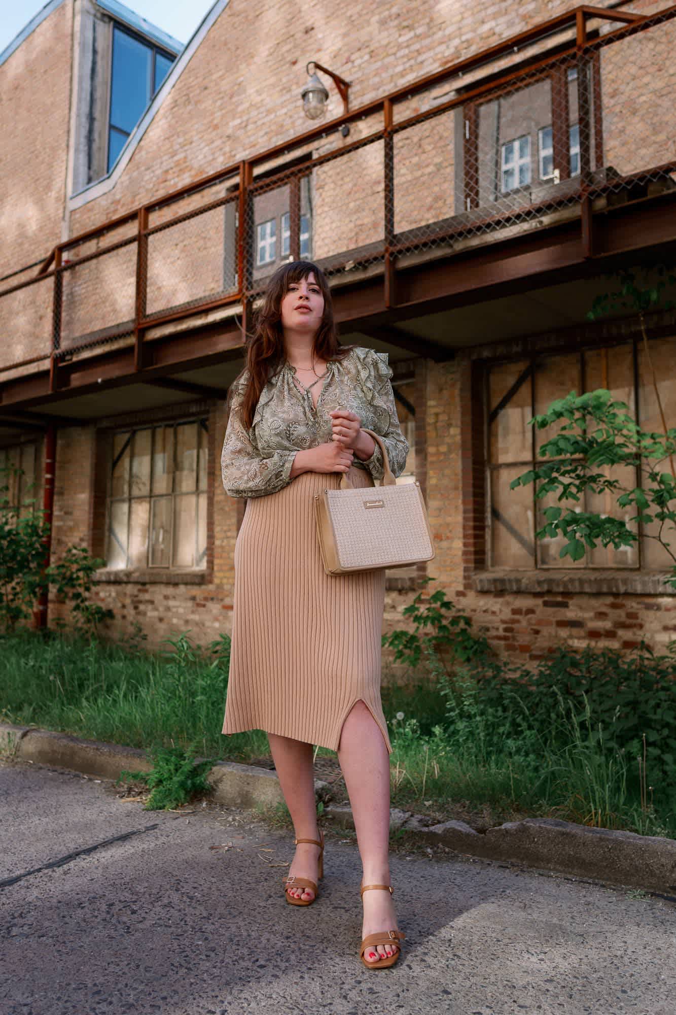 Frau trägt Midi-Rock und gemusterte Bluse, kombiniert mit beiger Handtasche