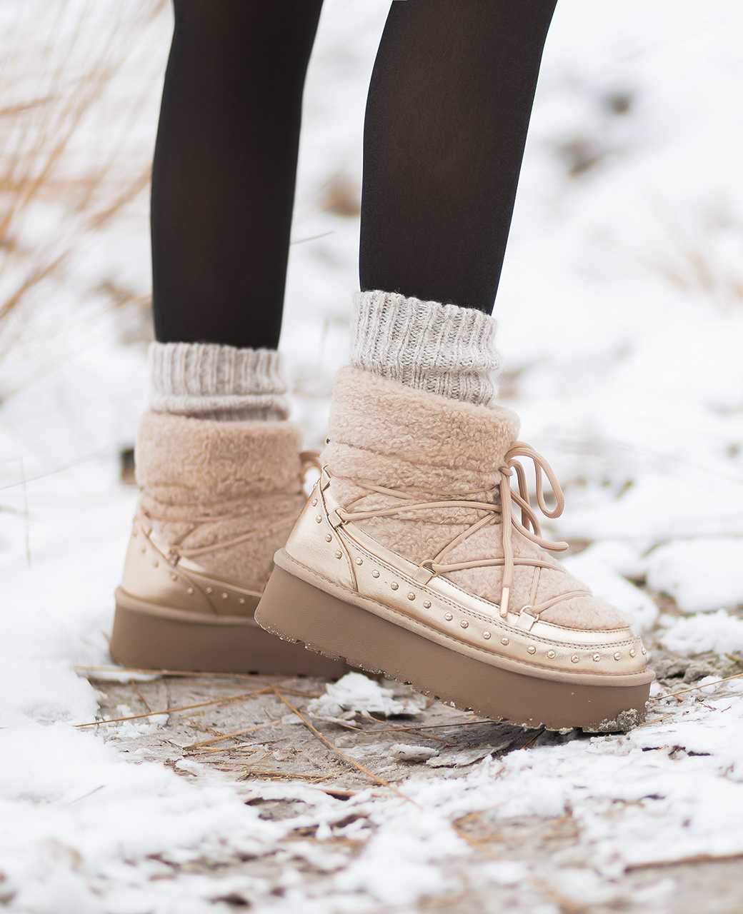 Person trägt beige Boots mit Kunstfell, zusammen mit schwarzer Leggings, stehend in Winterlandschaft