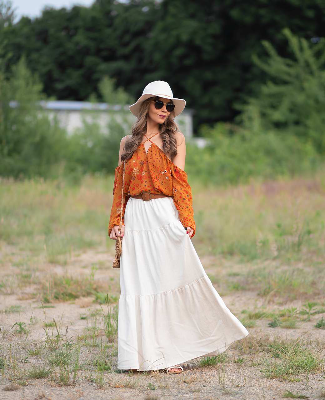 Frau in weißem Maxirock, kombiniert mit orangenem Top und weißem Hut, steht auf Wiese