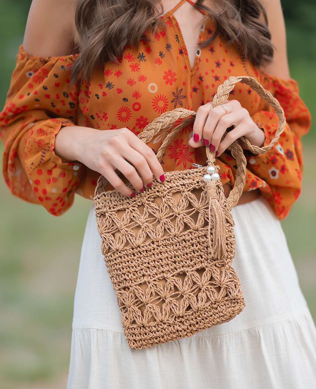 Frau mit orangenem Top und weißem Rock trägt Basttasche in der Hand