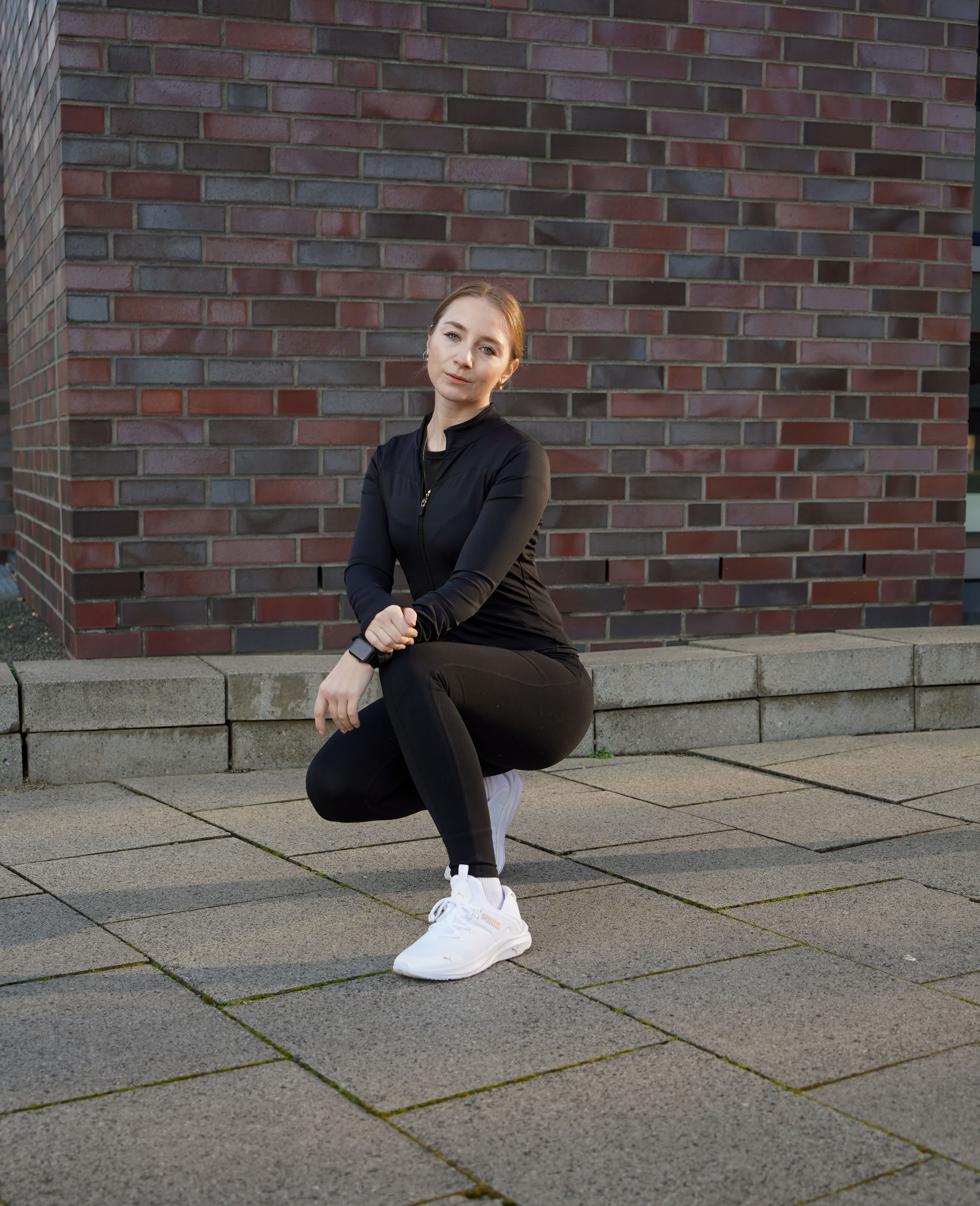 Frau mit schwarzem Sport-Outfit und weißen Sportschuhen in hockender Haltung