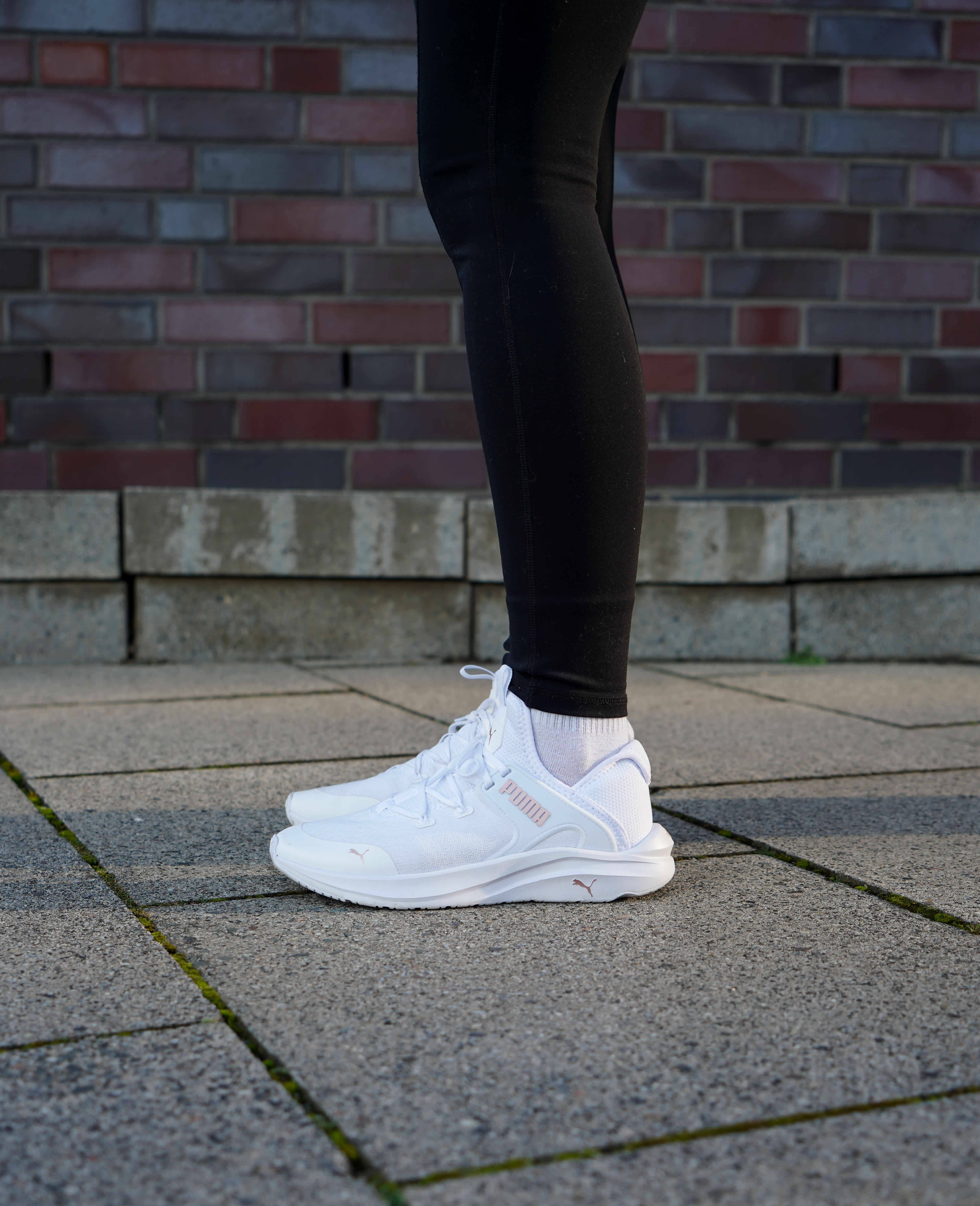 Nahaufnahme einer Person, die weiße Schuhe der Marke Puma und schwarze Sporthose trägt