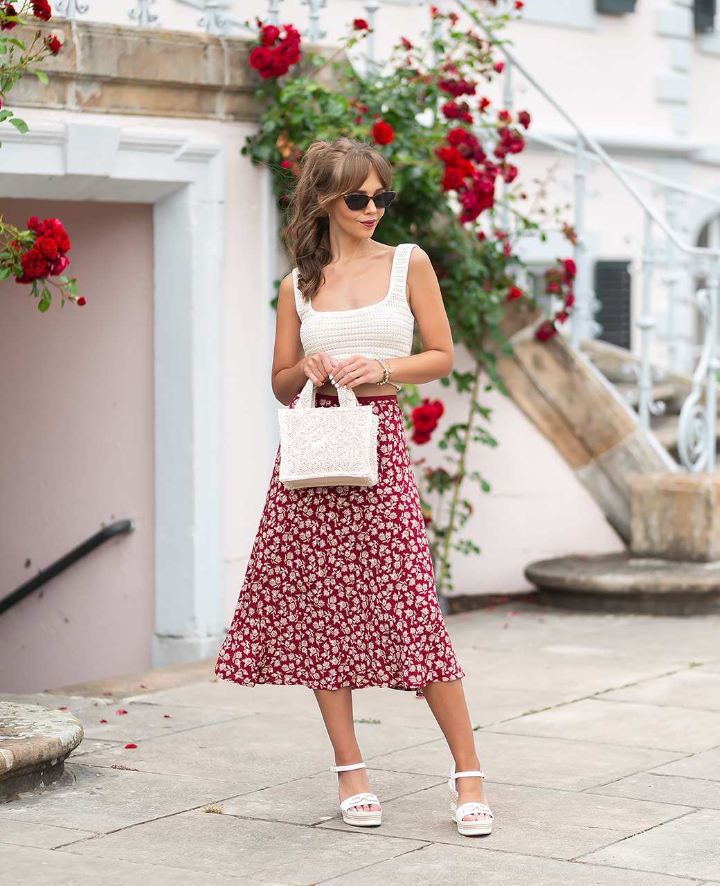 Frau mit weißem Top und rotem Kleidrock mit floralem Muster posiert mit weißer Boho-Tasche