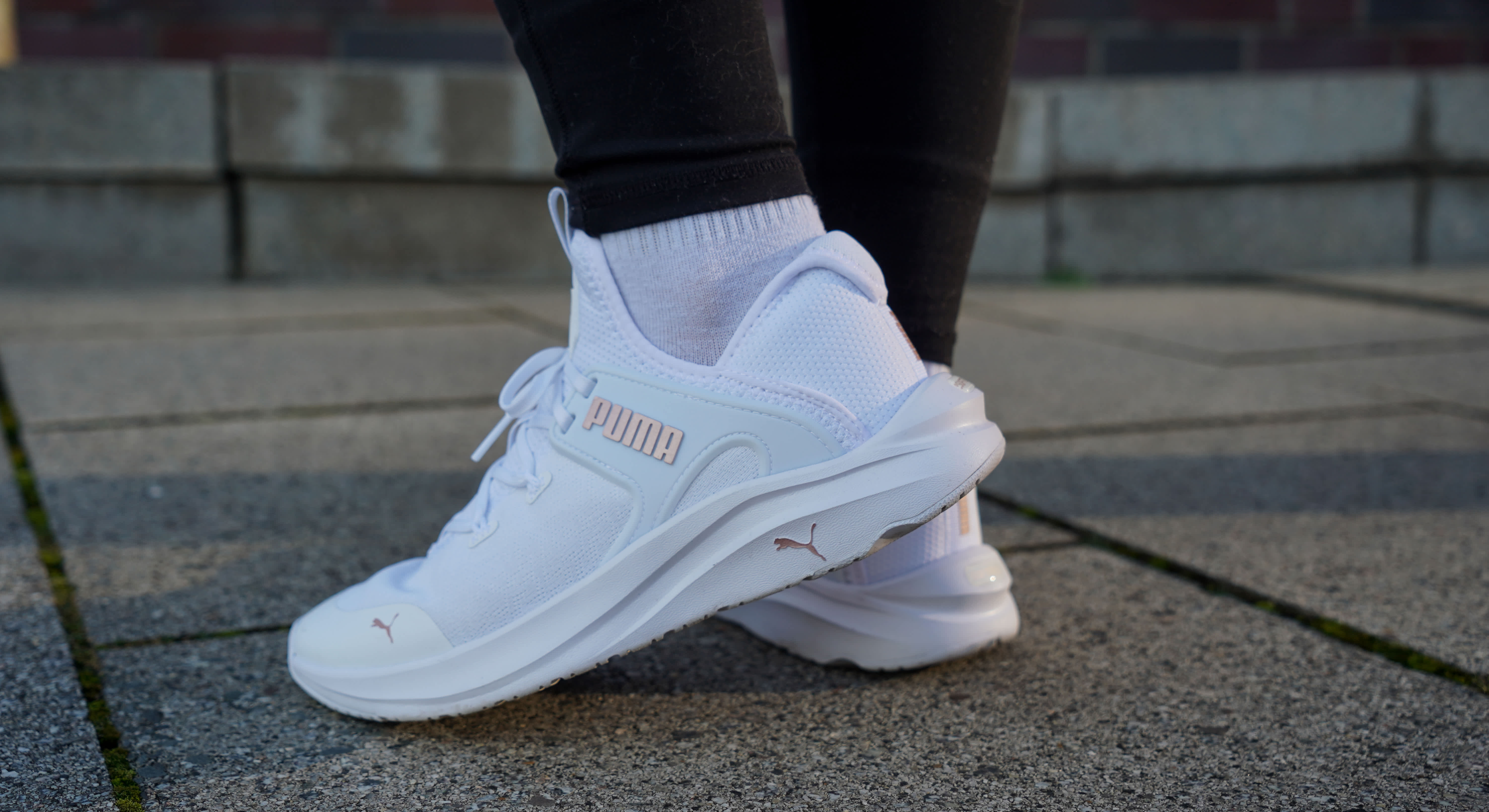 Nahaufnahme einer Person mit weißen Puma-Sportschuhen und schwarzer Sporthose