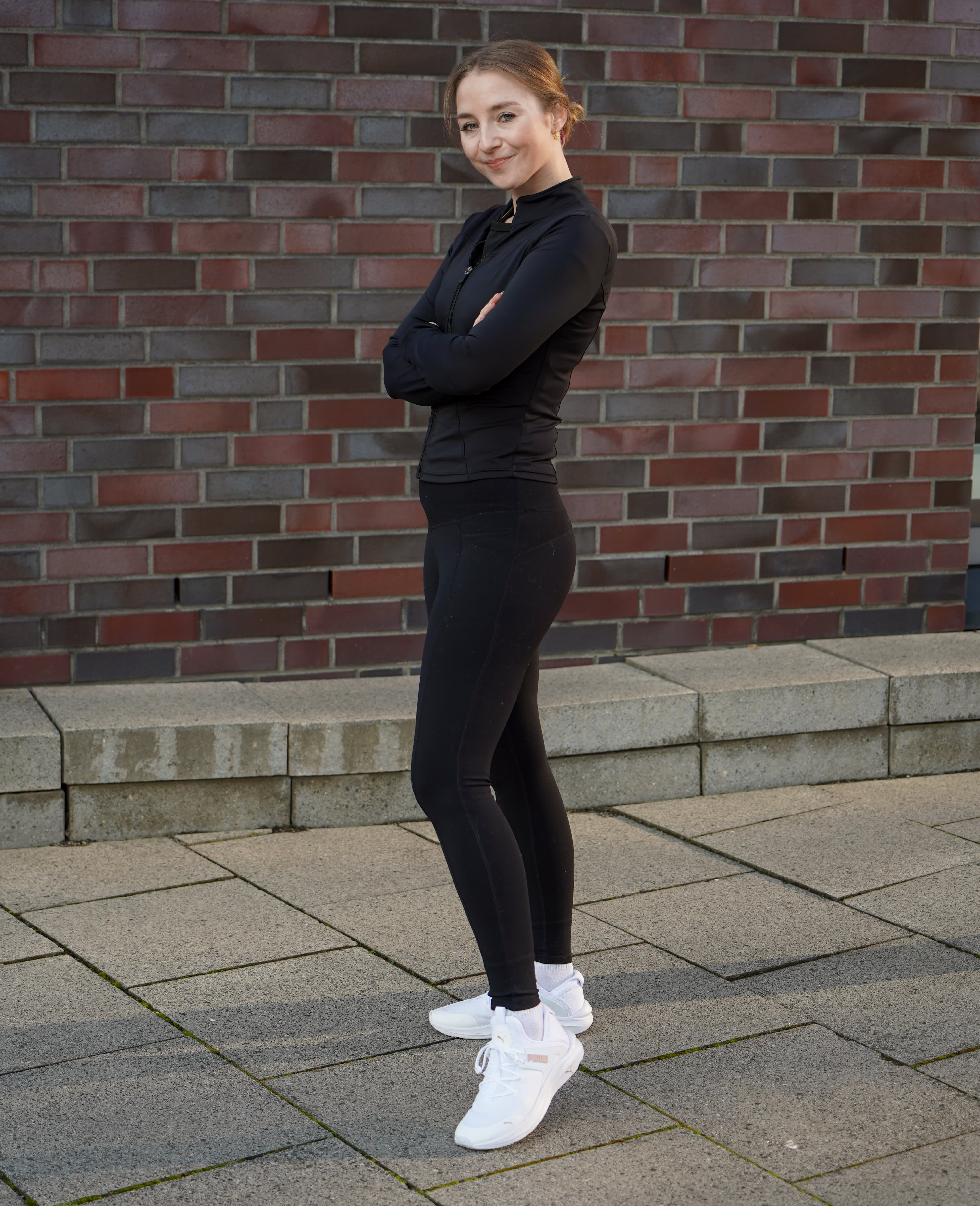 Frau in Winter-Sportoutfit aus schwarzem Oberteil mit passender Hose und weißen Laufschuhen