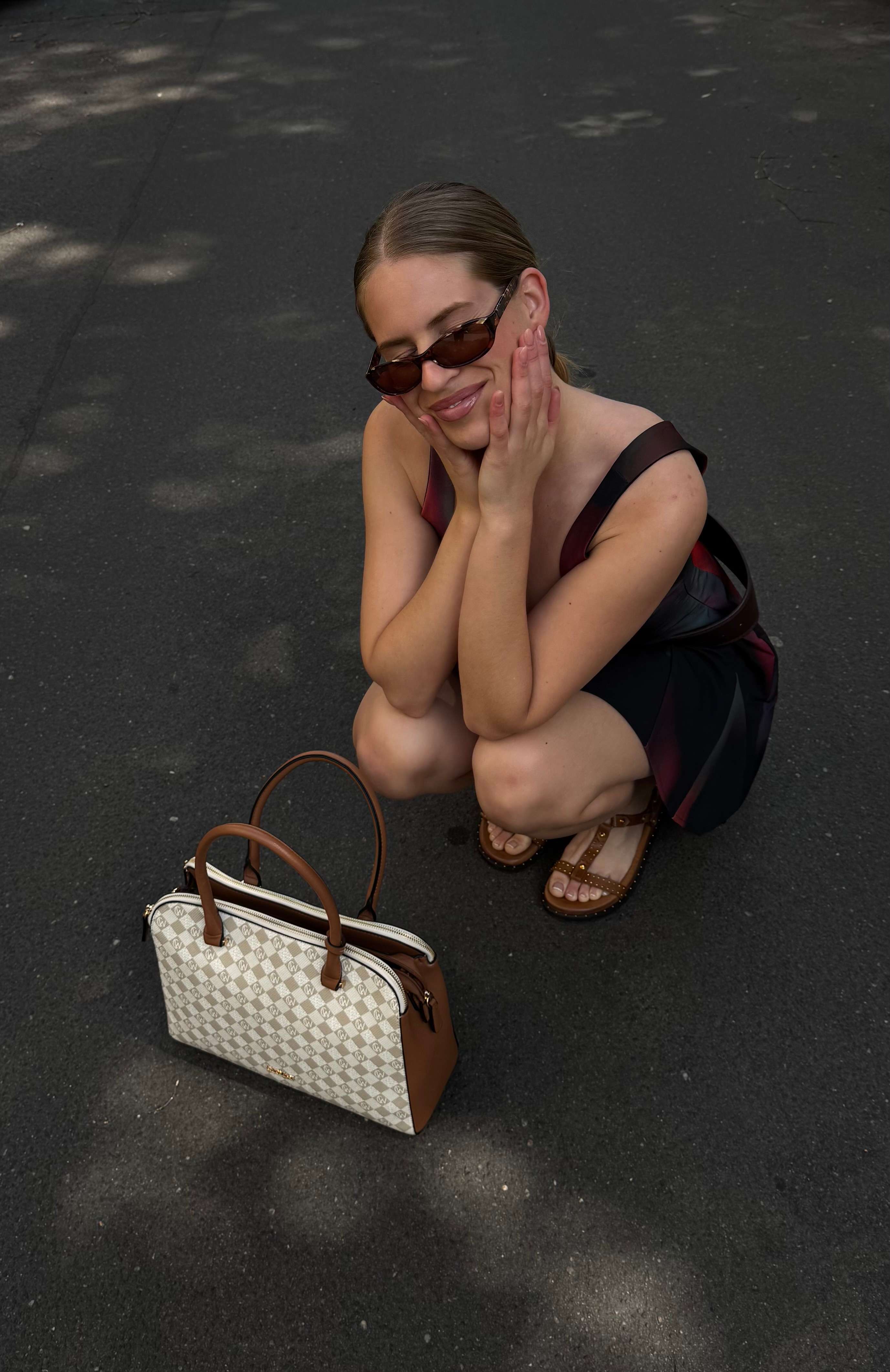 Frau in rotem Kleid, in gehockter Haltung auf Straße, vor ihr steht eine elegante Tasche