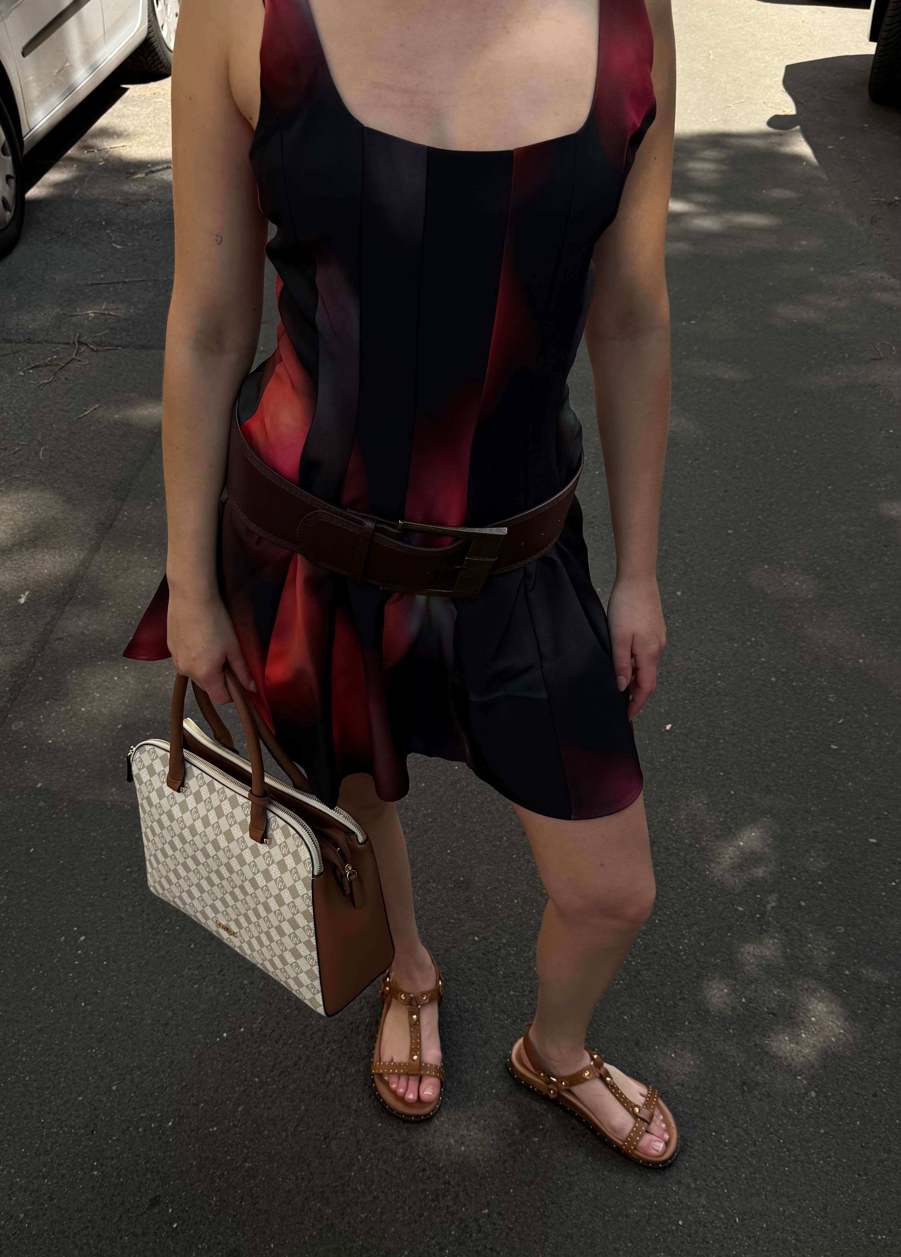 Frau steht lässig in rotem Sommerkleid, kombiniert mit weißer Handtasche und offenen Riemchen-Sandalen