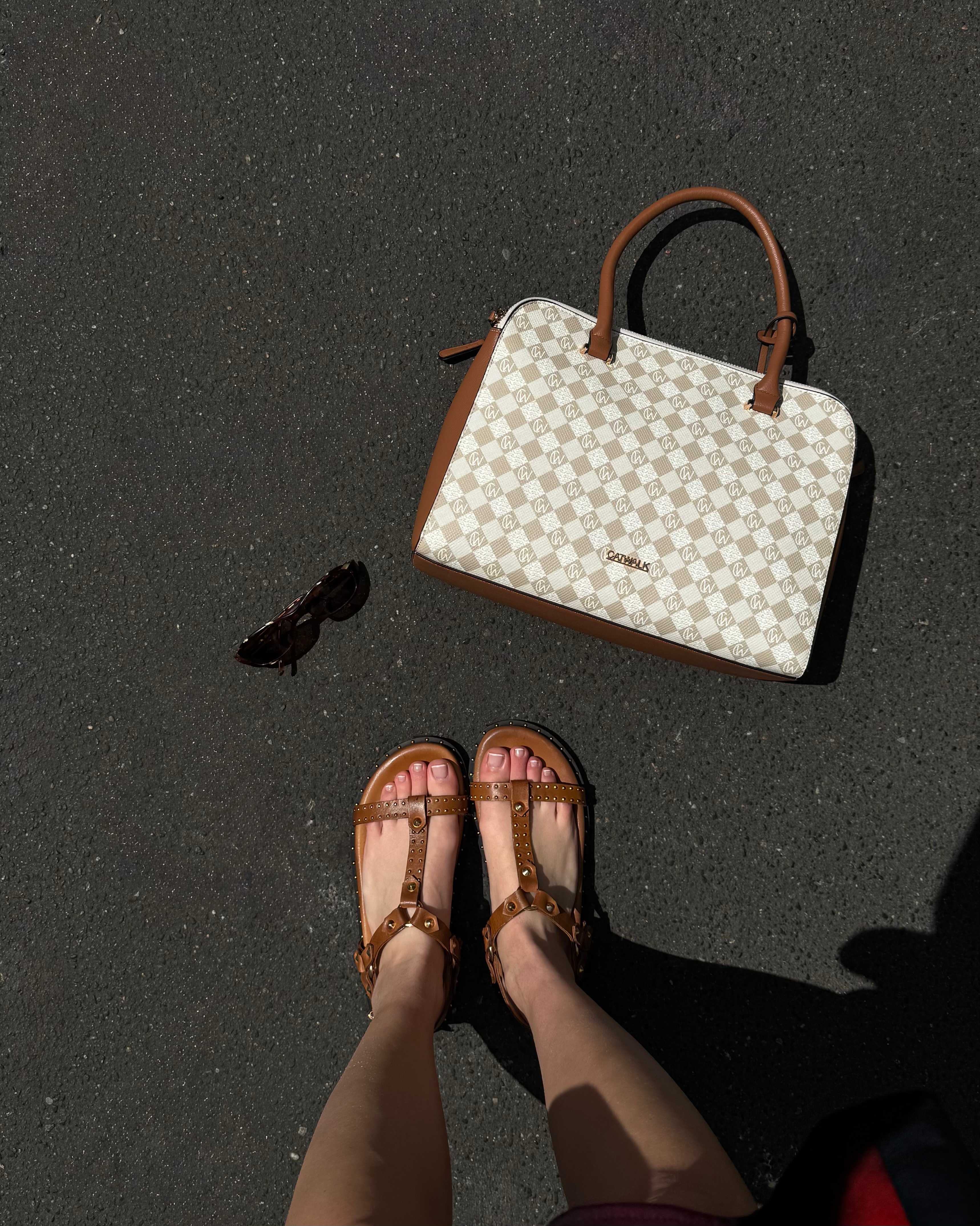 Top-Down-Ansicht einer Person, die offene Sandalen mit Riemchen trägt, davor liegt weiße Handtasche
