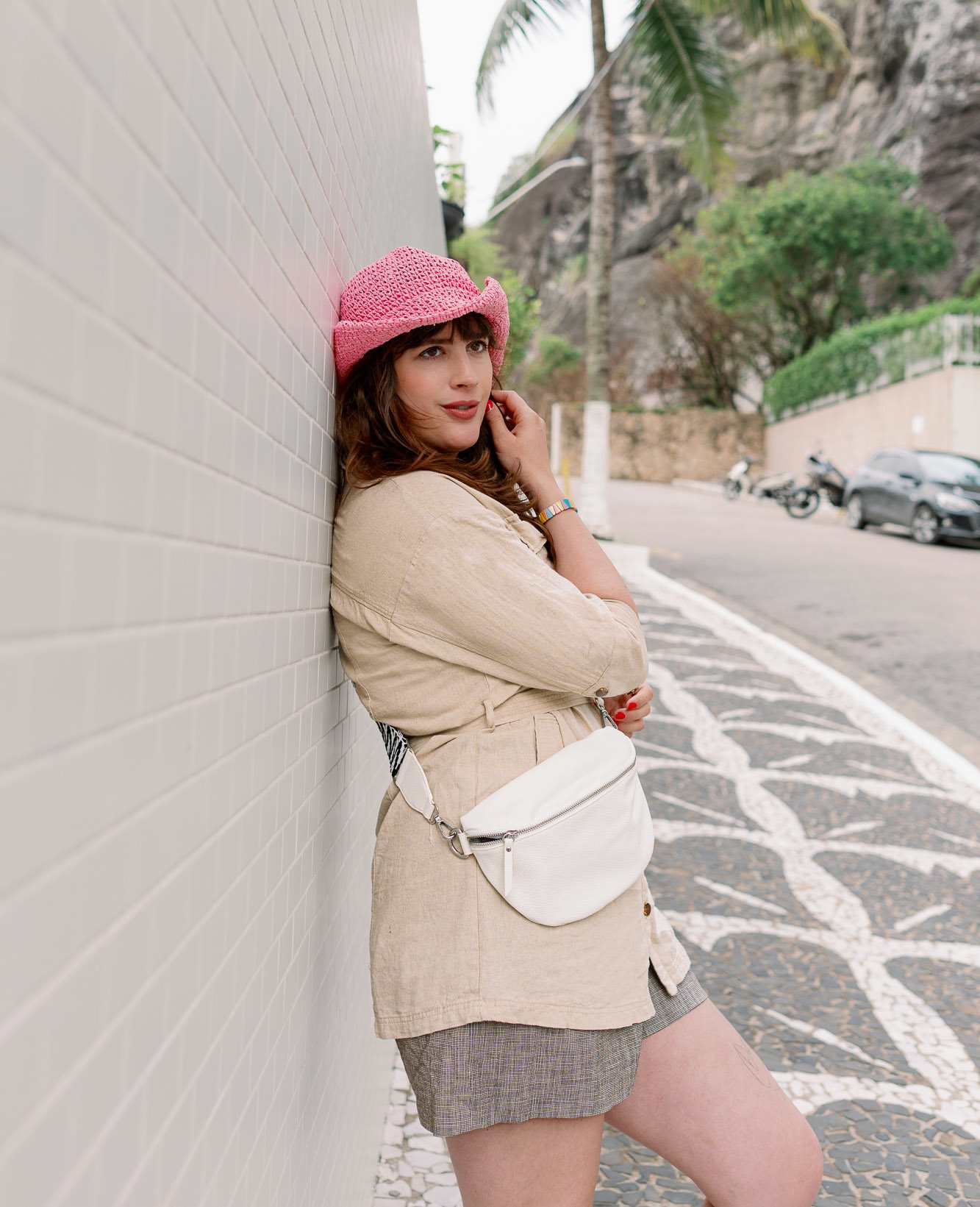 Frau präsentiert ihren pinken Strohhut, sie lehnt lässig gegen eine Wand 