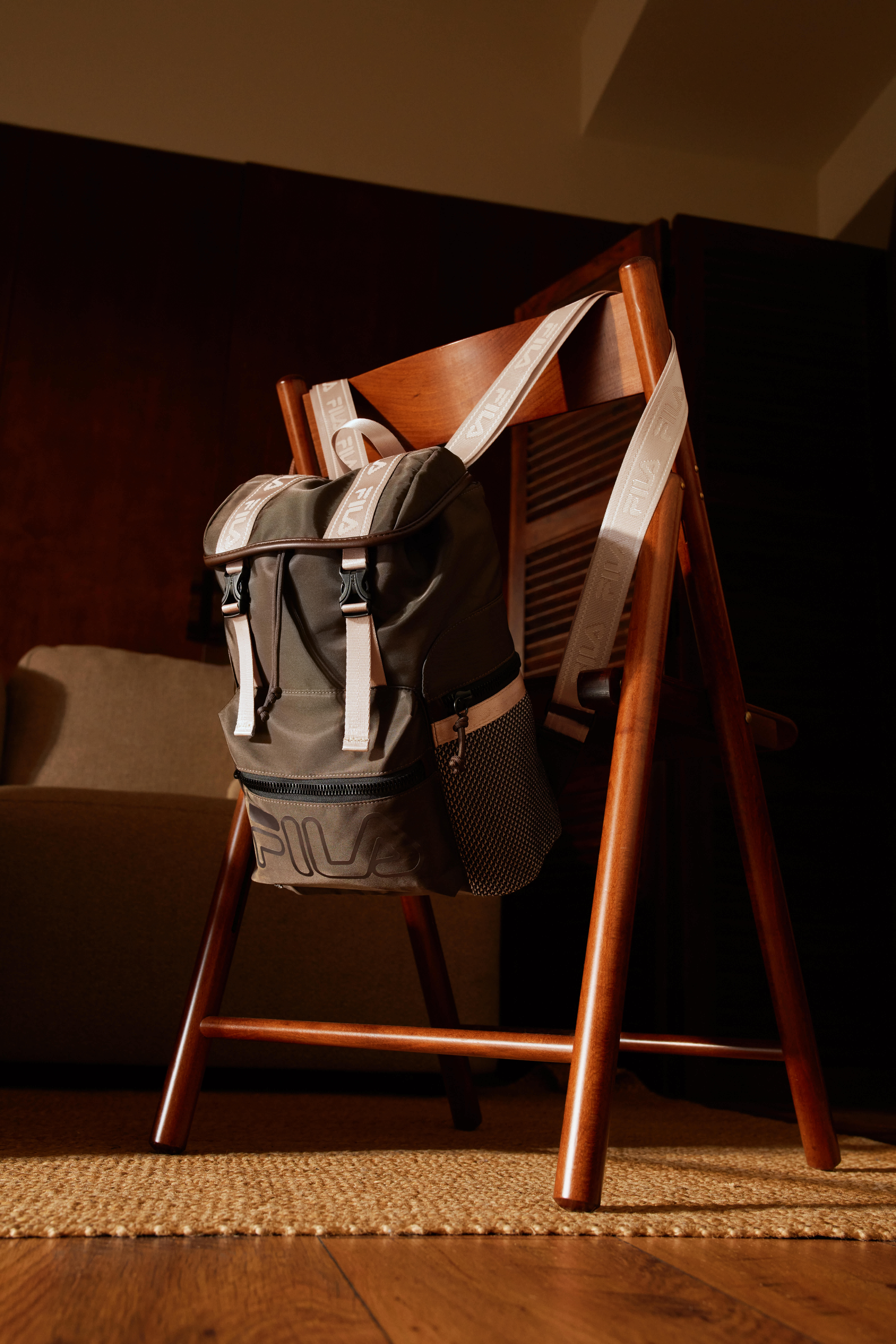 Ein olivgrüner FILA-Rucksack hängt an einem Holzstuhl