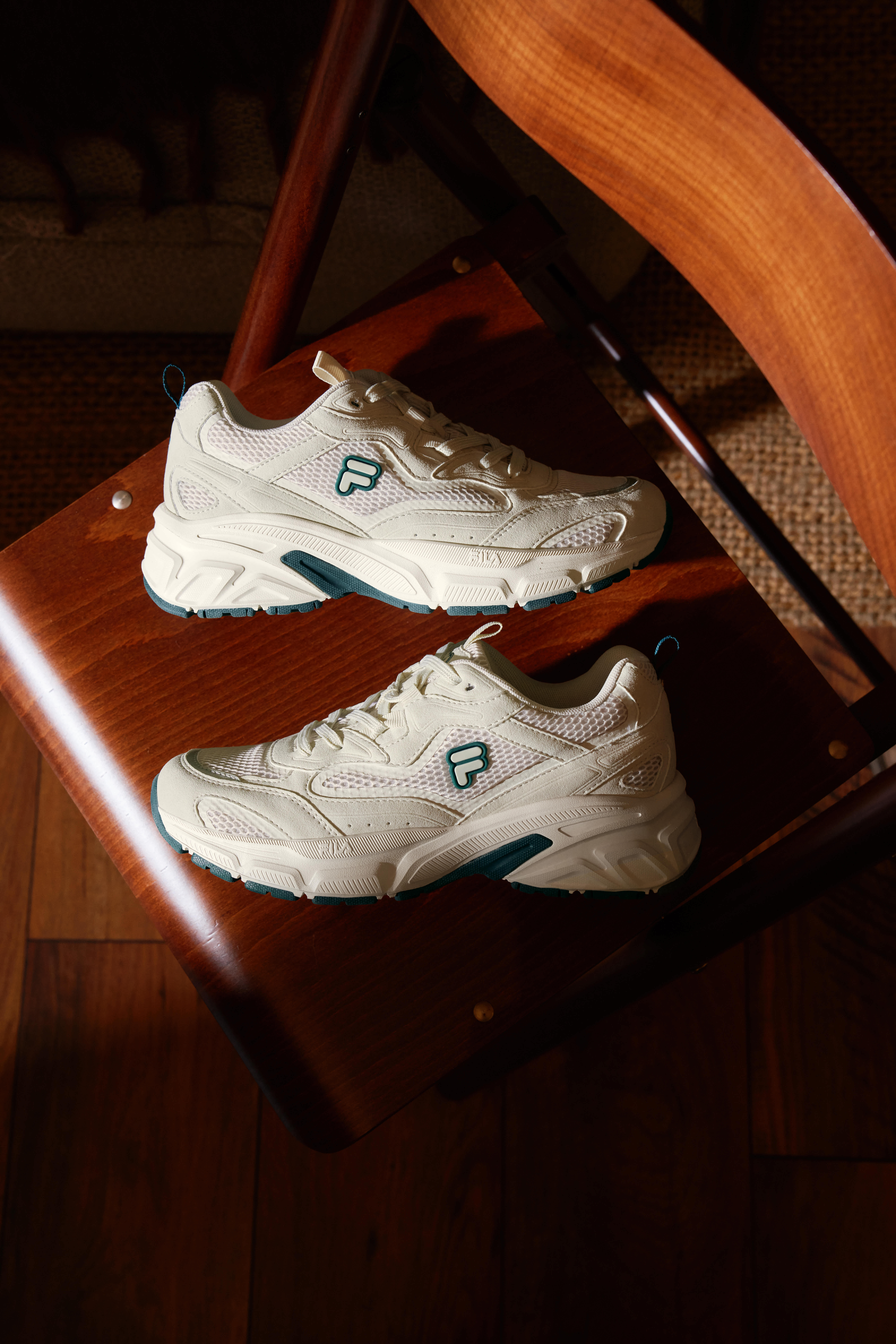 Ein Paar weiße FILA-Sneaker mit dunkelgrünen Details liegen auf einem Holzstuhl