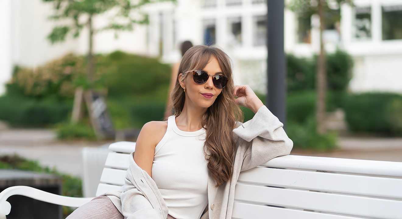 Junge Frau sitzt auf weißer Bank, trägt passendes Outfit im Scandi Style