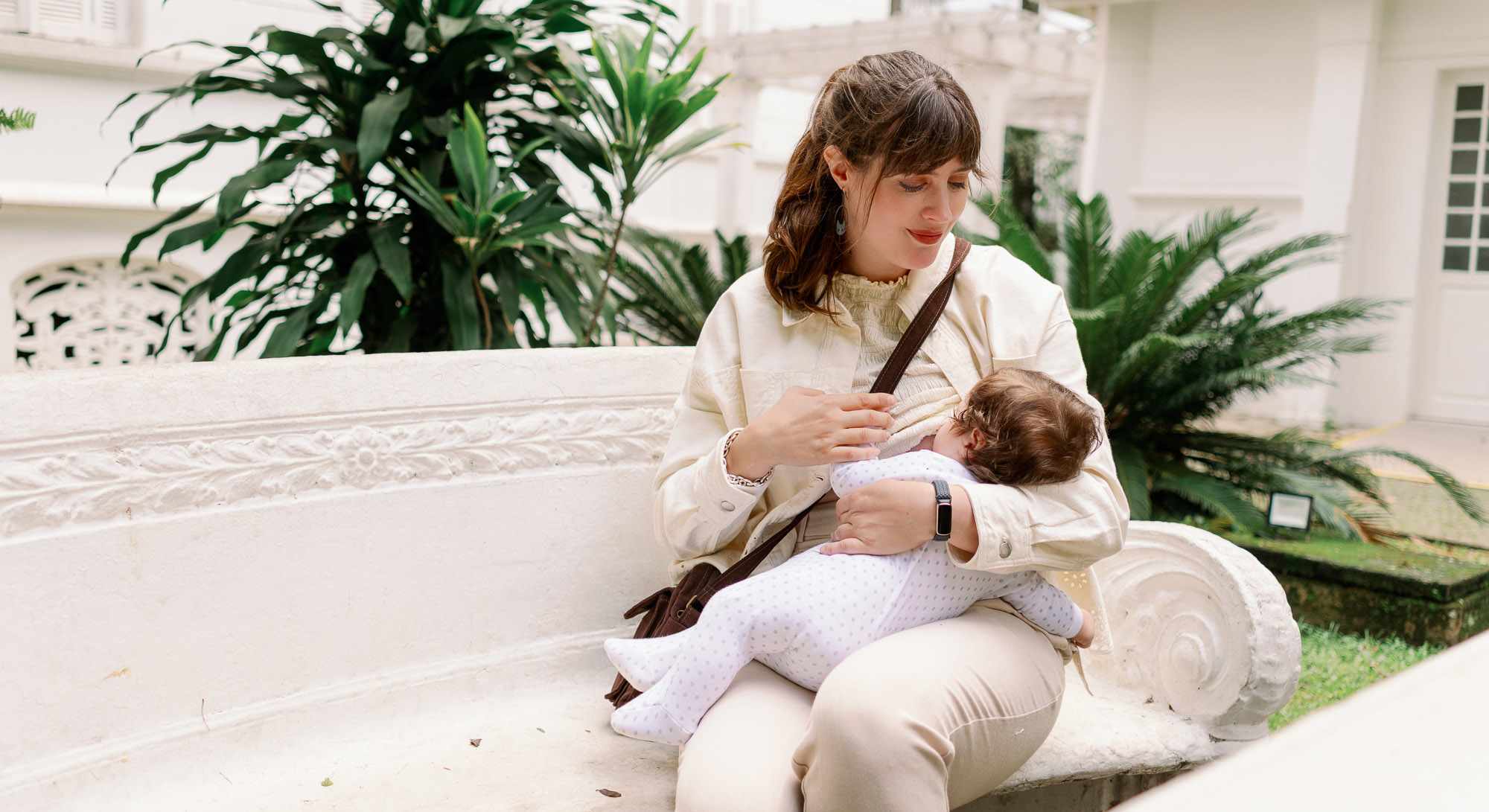 Frau sitzt auf weißer Steinbank mit Baby auf dem Arm