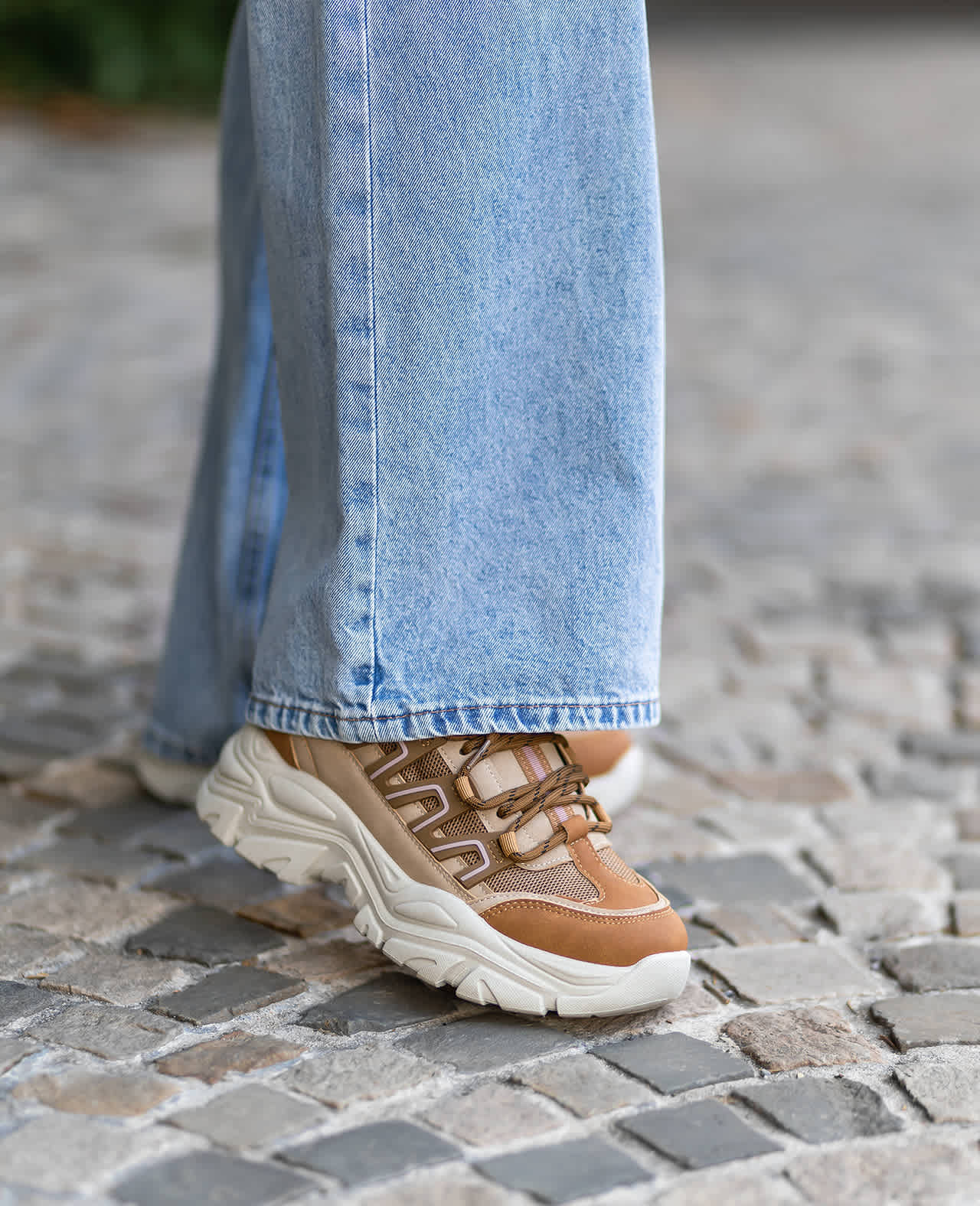 Frau trägt braune Chunky Sneaker in Kombination mit blauer Jeanshose