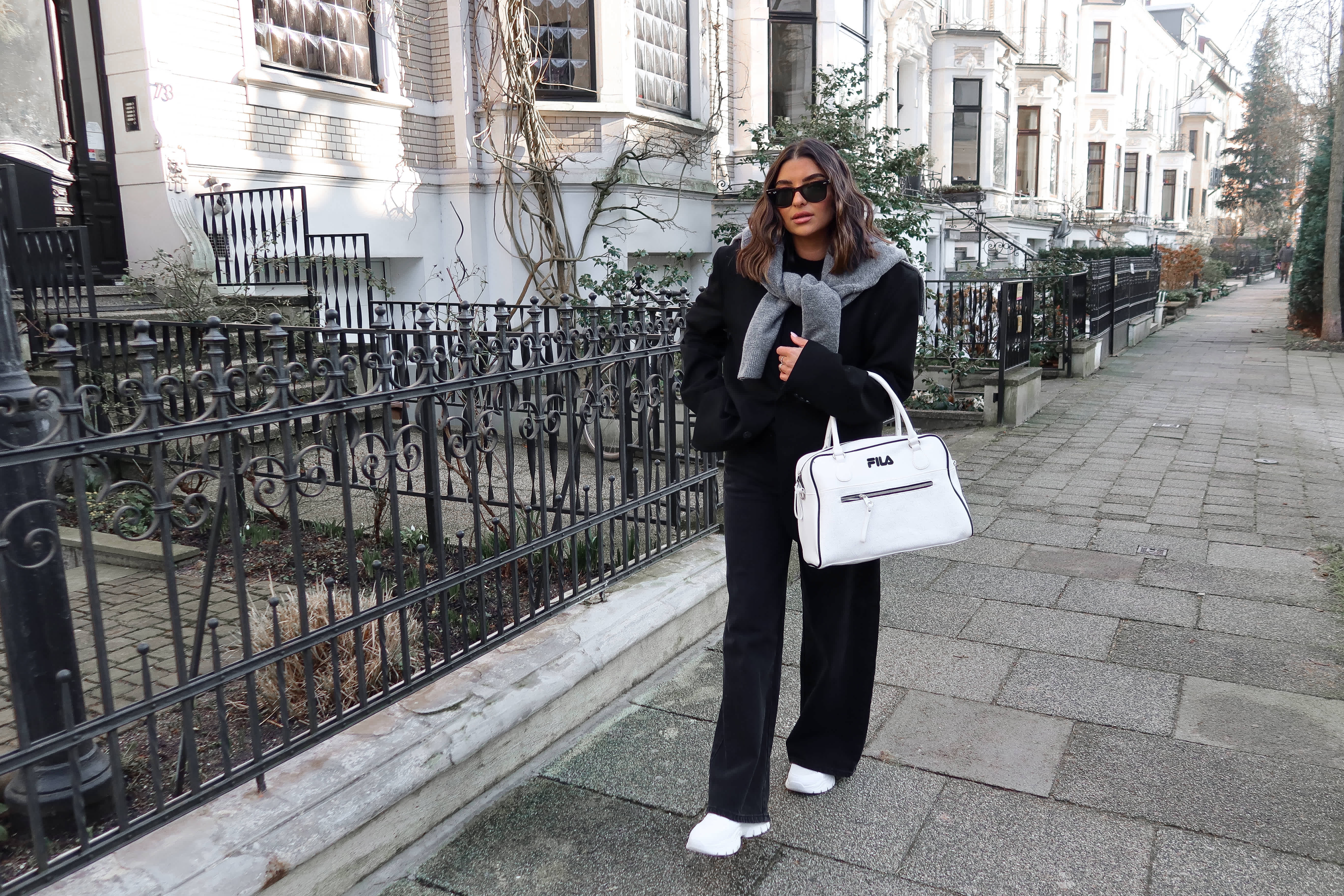Frau spaziert auf Fußweg, gekleidet in warmes Outfit mit weiter Hose und FILA-Handtasche